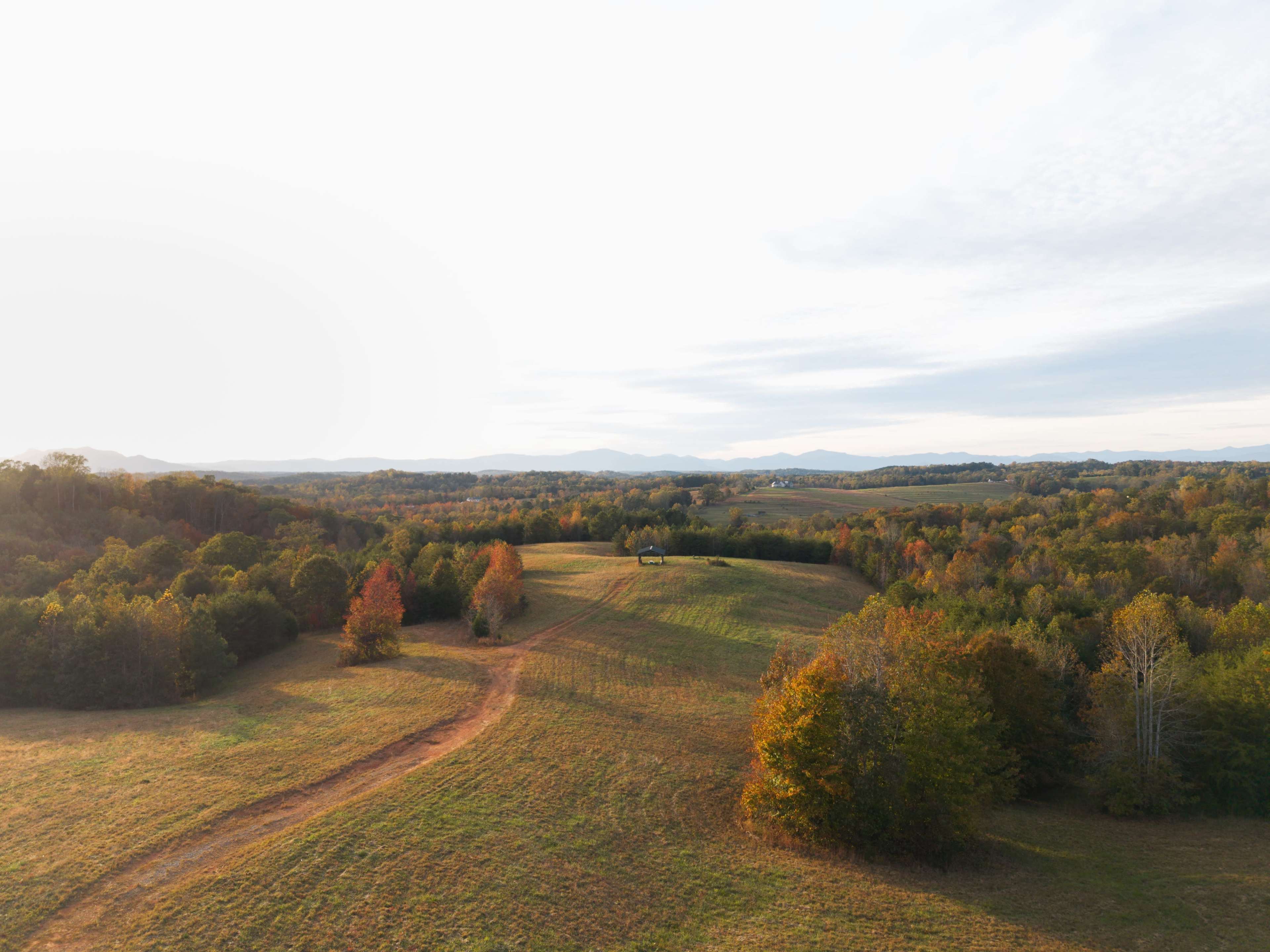 A distant farm is nestled among rolling hills and autumn-colored trees under a cloudy sky.