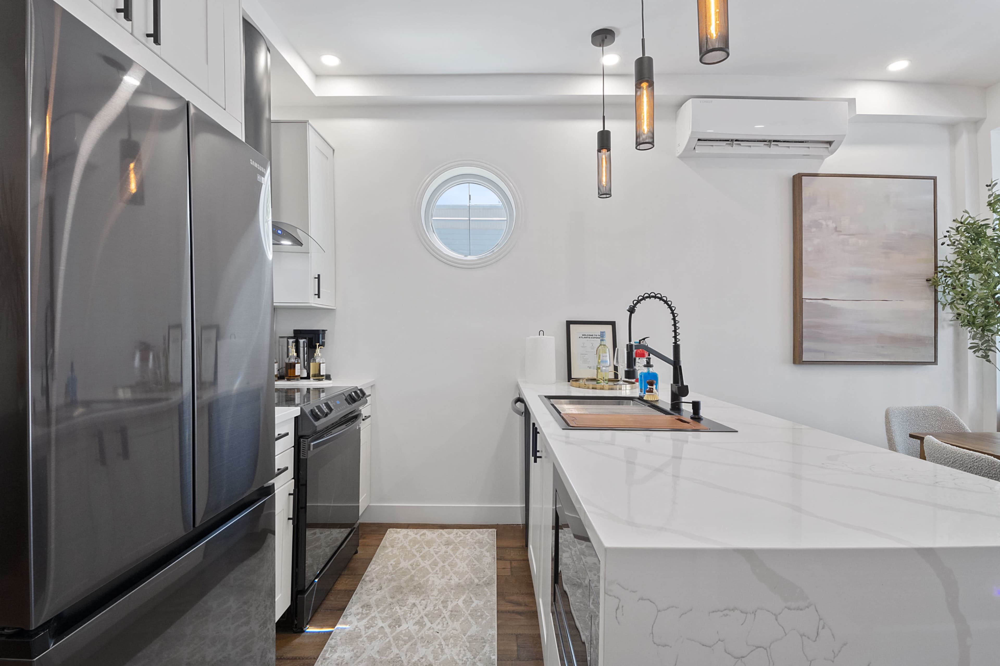 A modern kitchen features a central island with a sink and stovetop, surrounded by stainless steel appliances and a circular window.