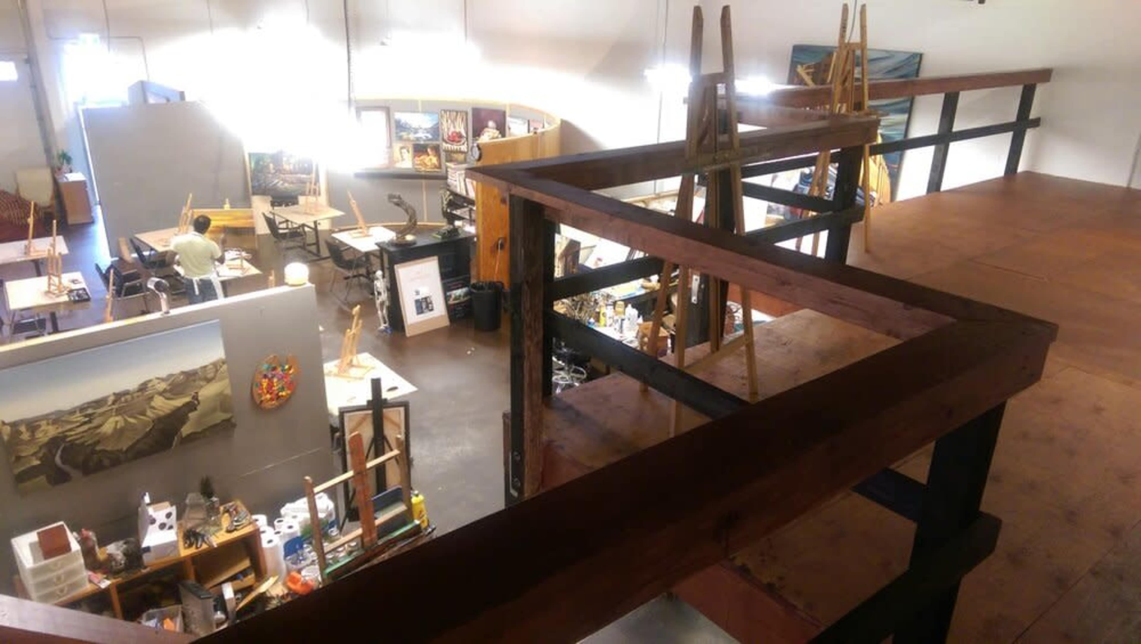 An art studio featuring easels, art supplies, and various artworks in a multi-level space with an elevated walkway overlooking the area.