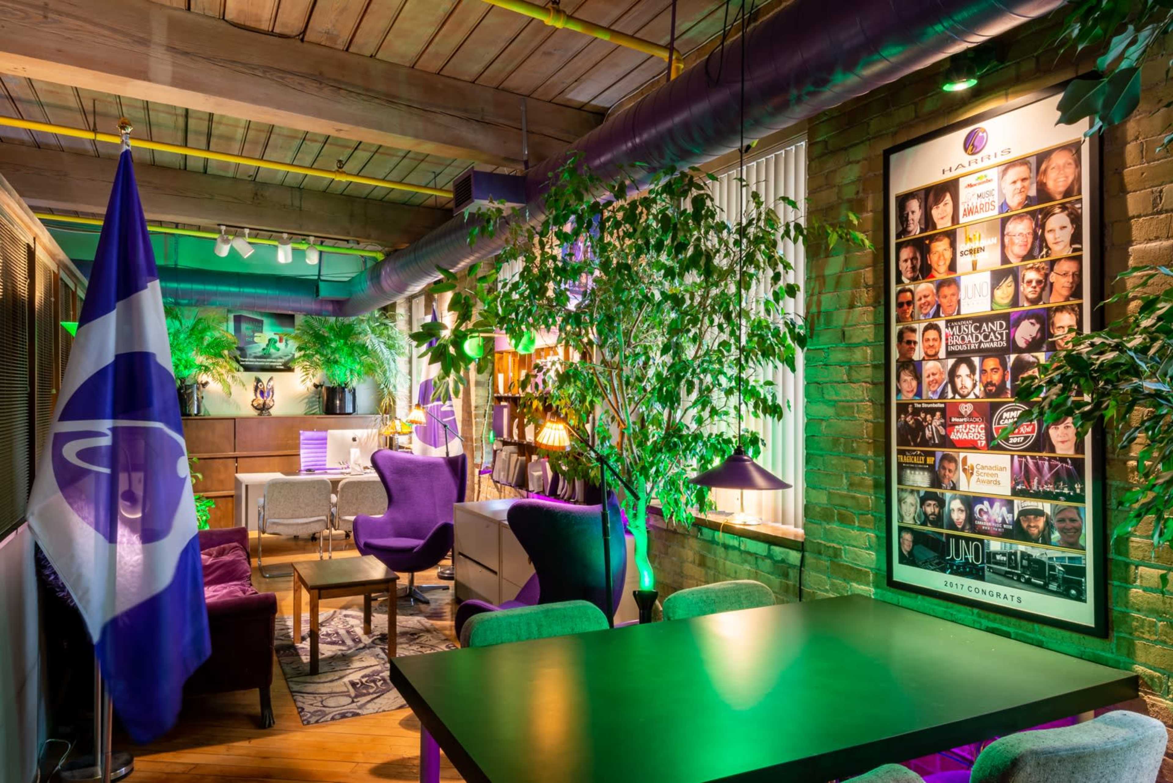 A modern, well-decorated room featuring plants, a table, seating areas, and a wall adorned with various framed images and posters.