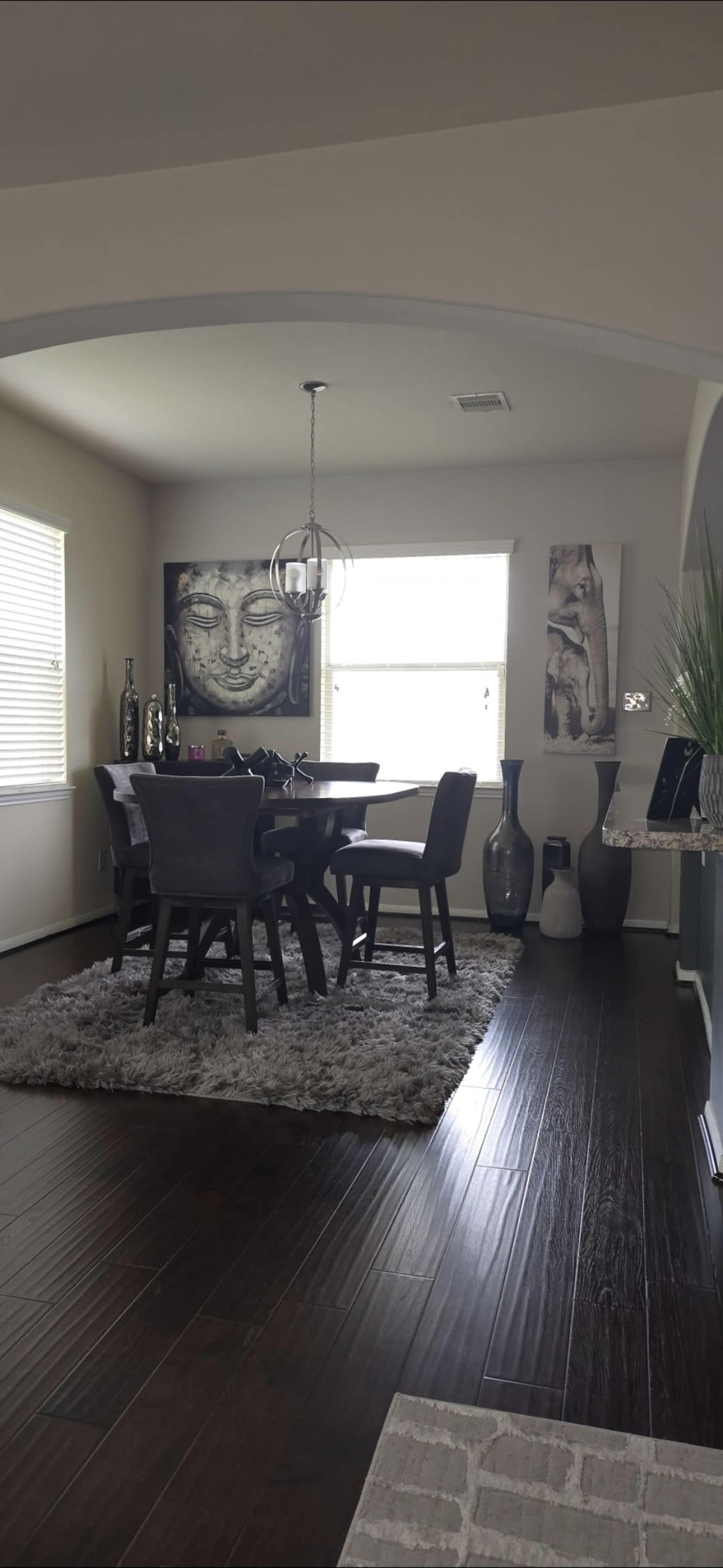 A dining area features a table surrounded by chairs, with a large wall art piece depicting a face and decorative vases enhancing the decor.
