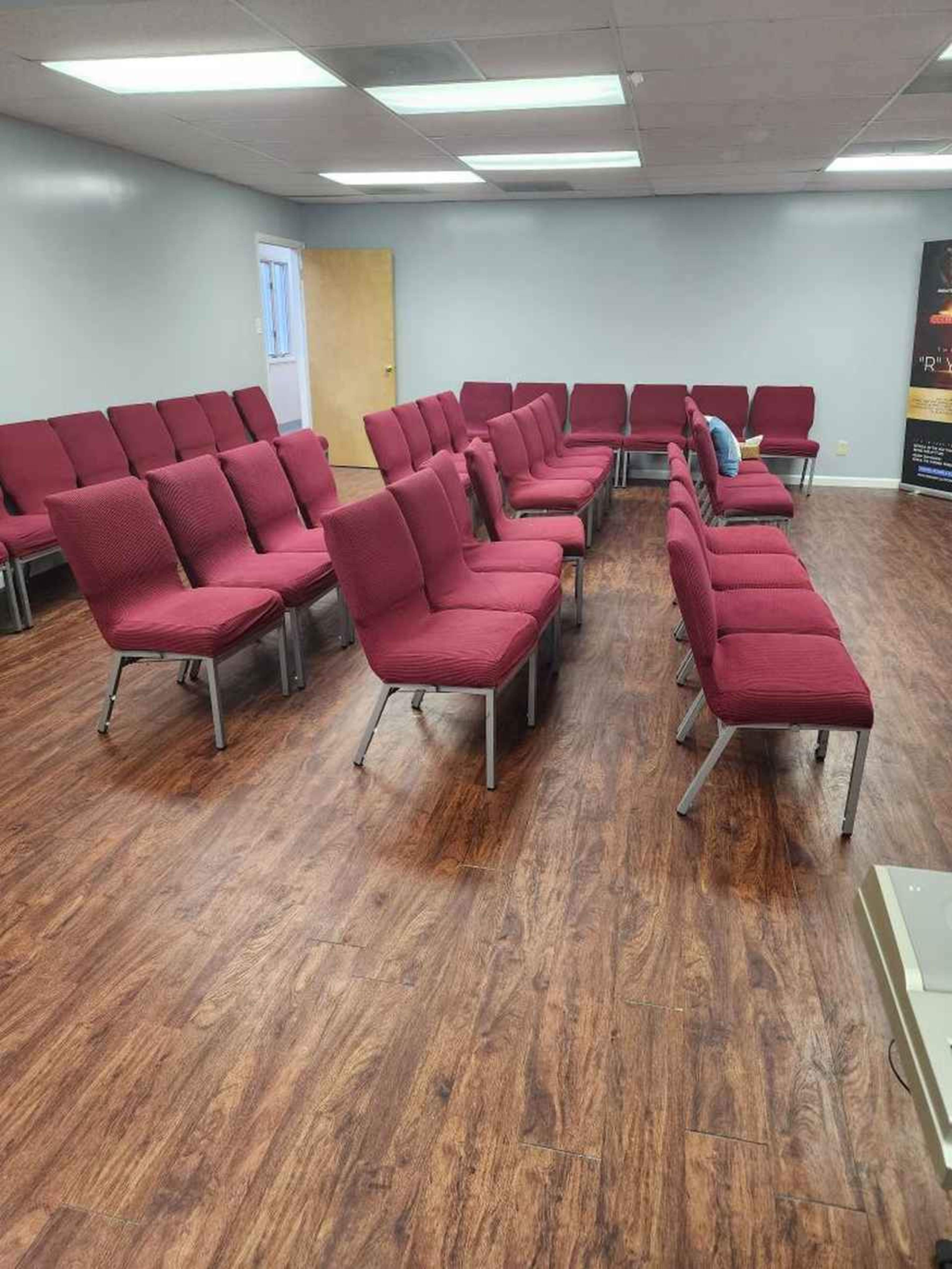 A room with rows of red chairs arranged in a semi-circle on a wooden floor.