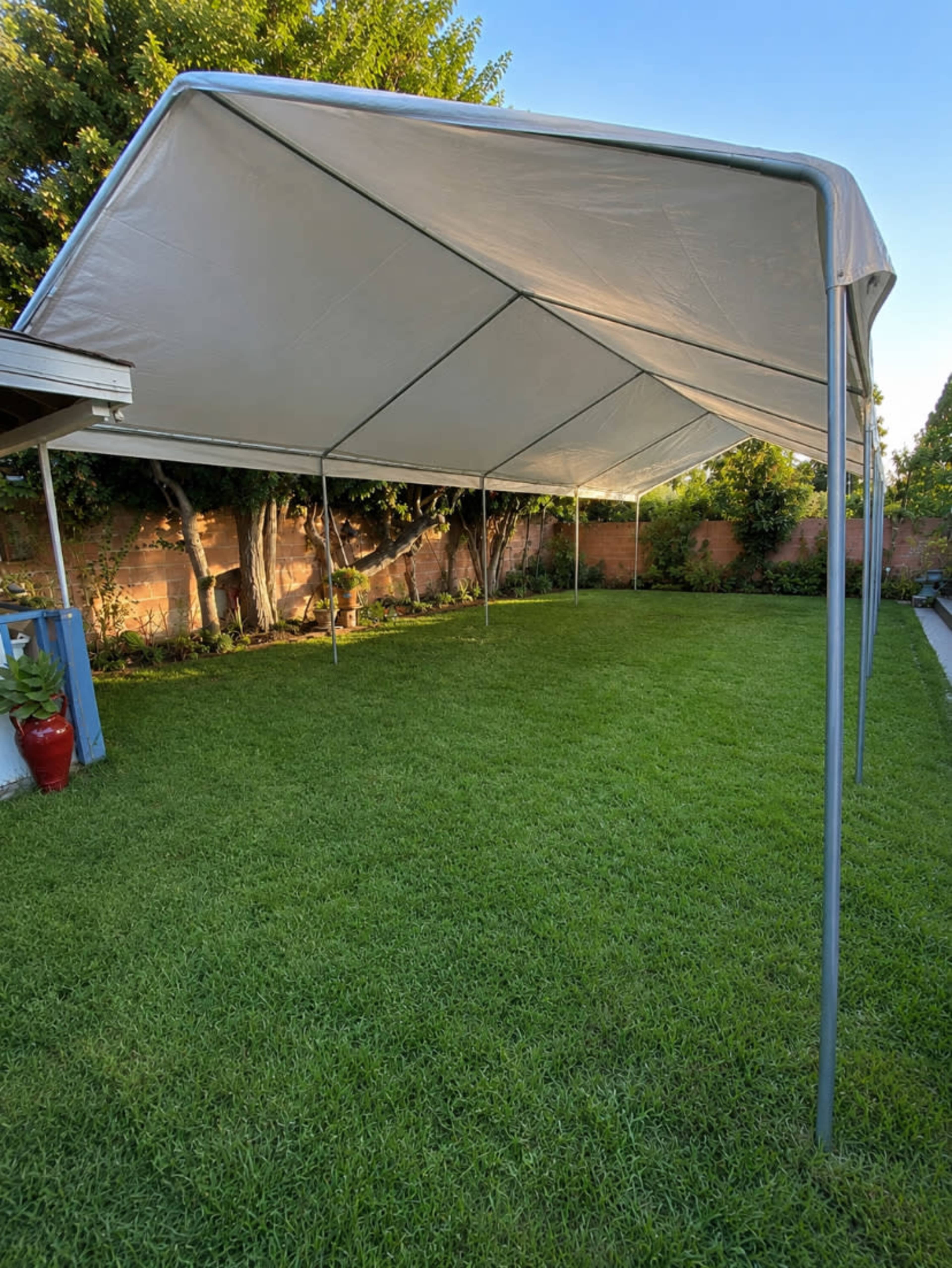 A large white canopy tent is set up on a green lawn surrounded by trees and bushes.