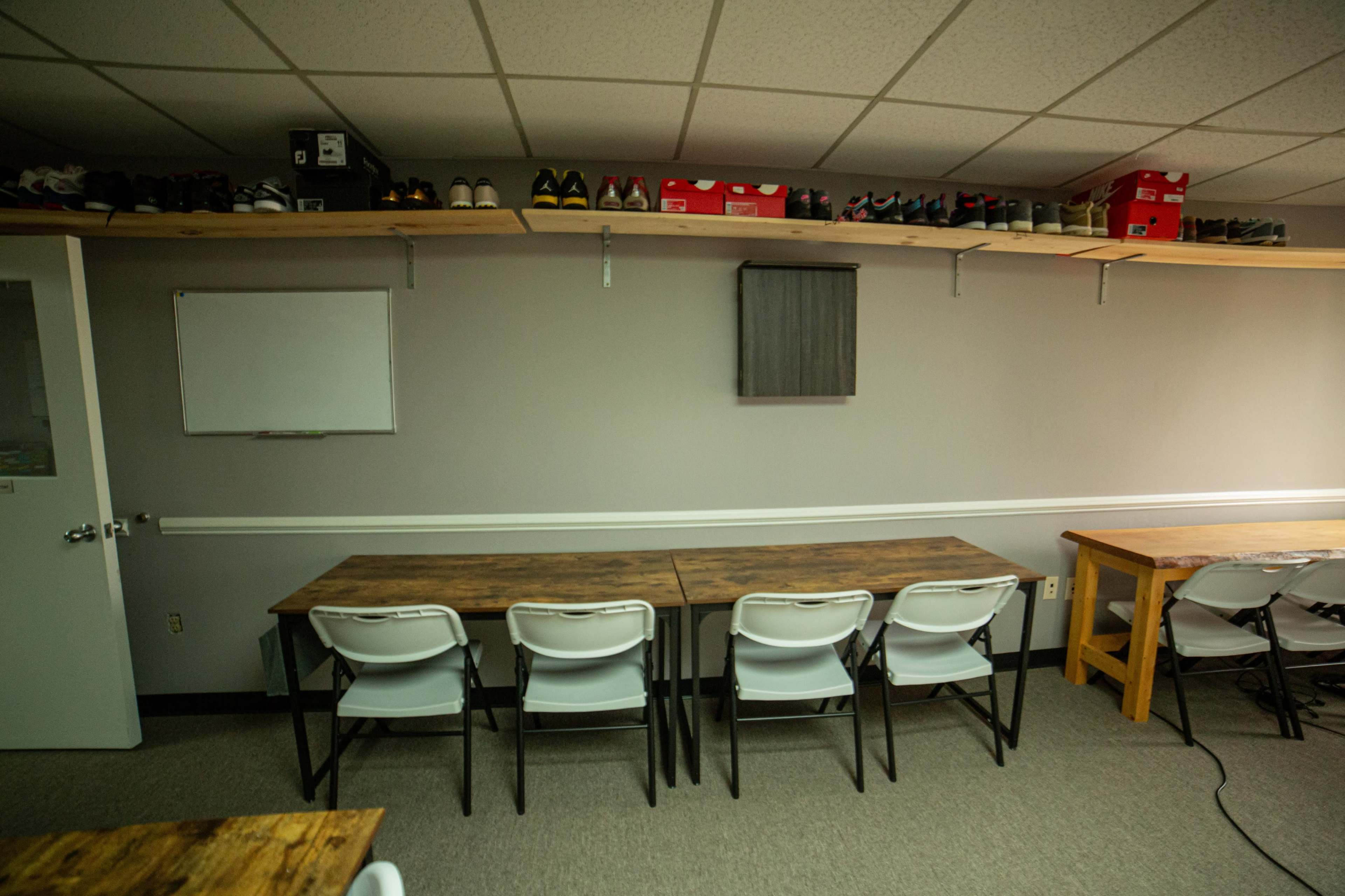 A minimalist room with two long tables and several pairs of shoes arranged on a shelf above.