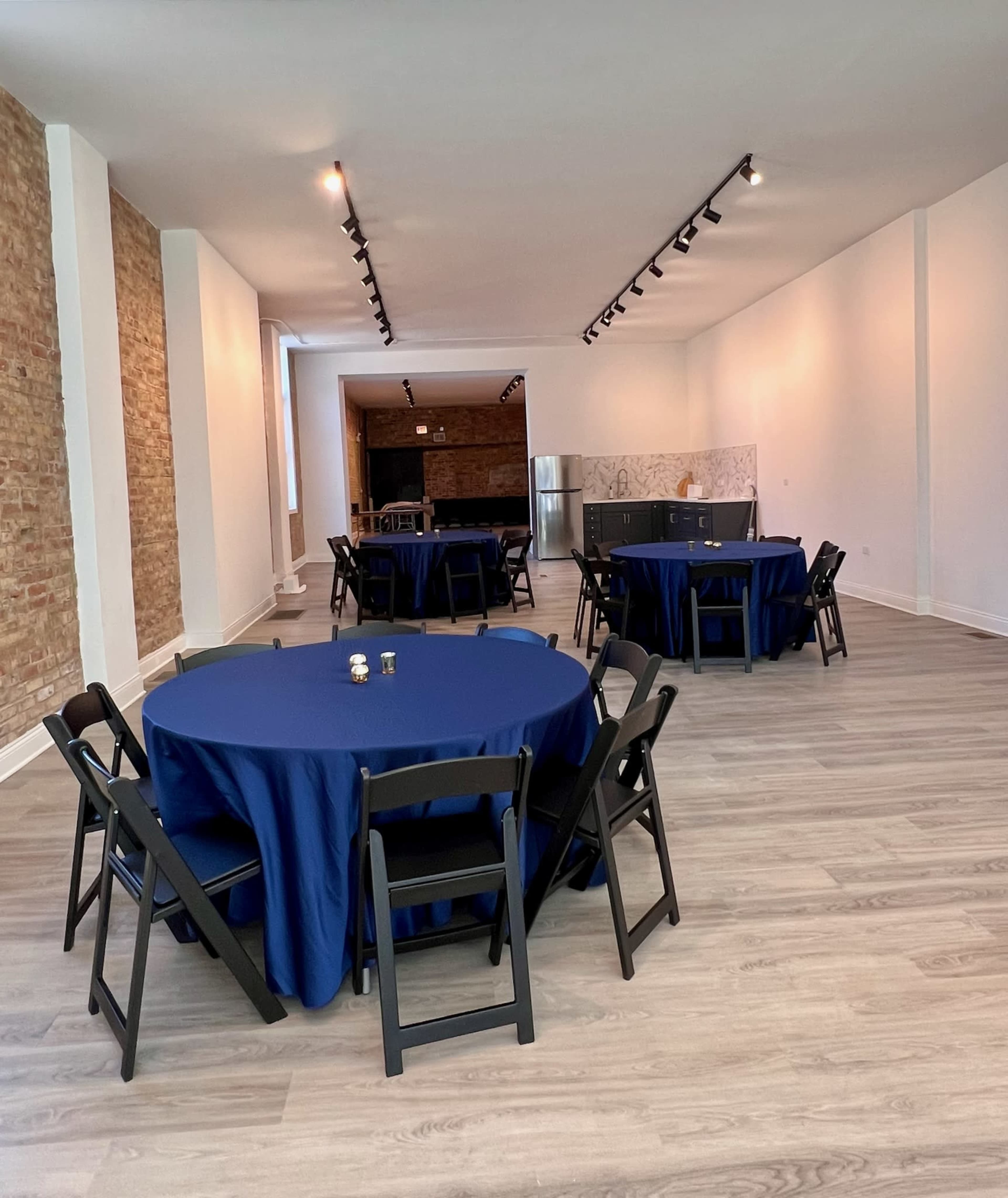 A spacious room with several round tables covered in navy blue tablecloths and black chairs arranged around them.