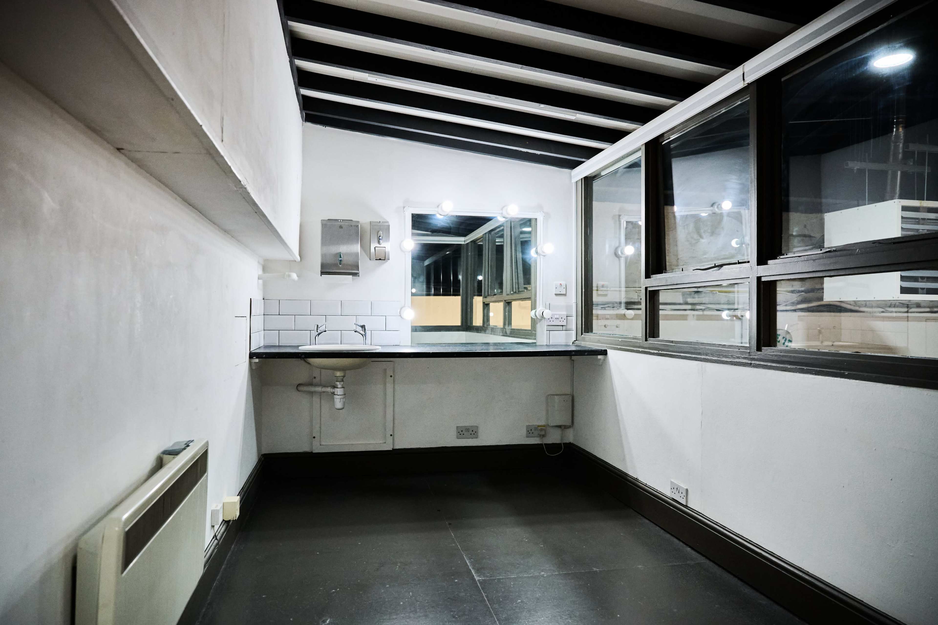 The image shows an empty room with a sink and large windows, featuring exposed beams along the ceiling.