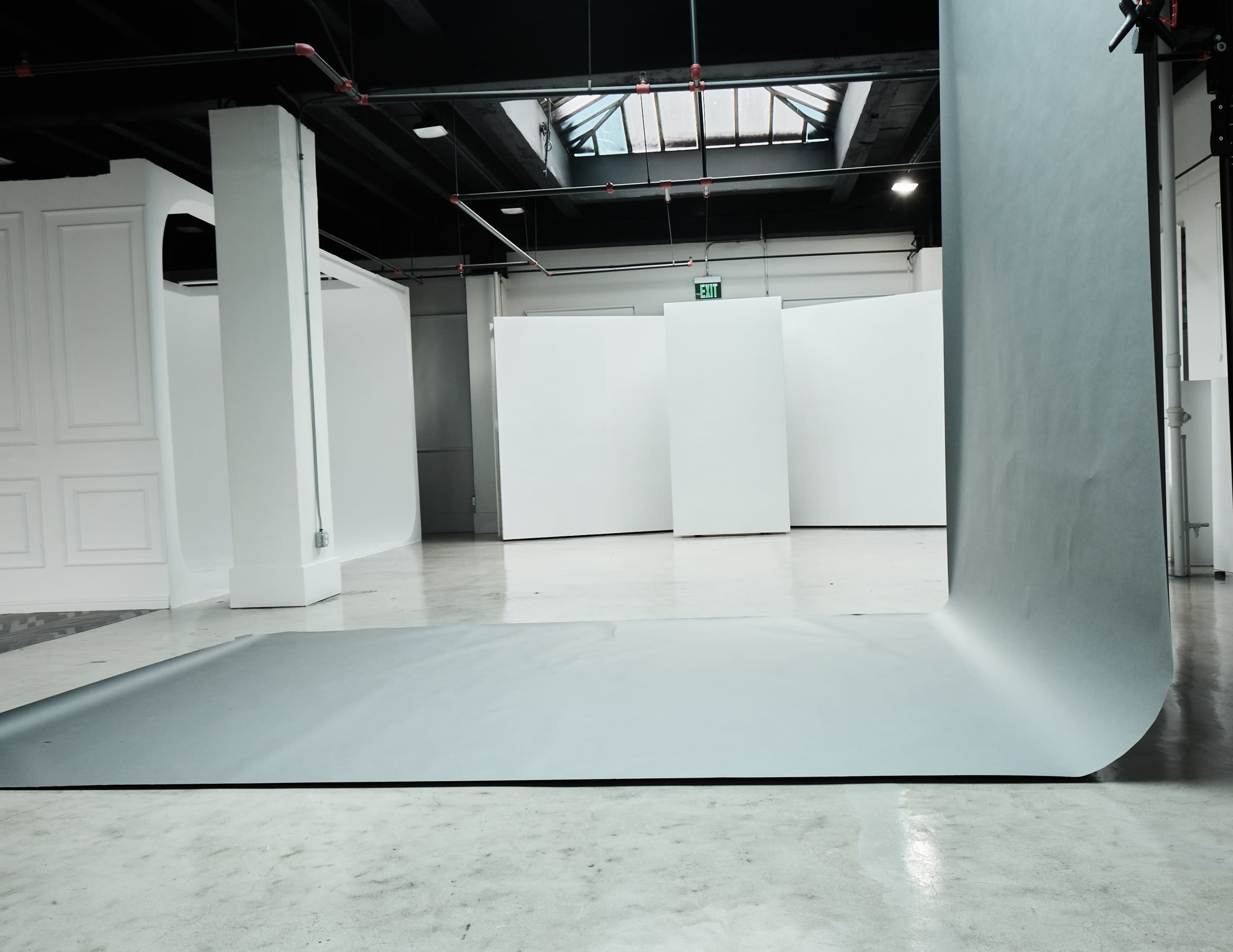 A spacious studio filled with white backdrops and a rolled-out gray background on the floor.