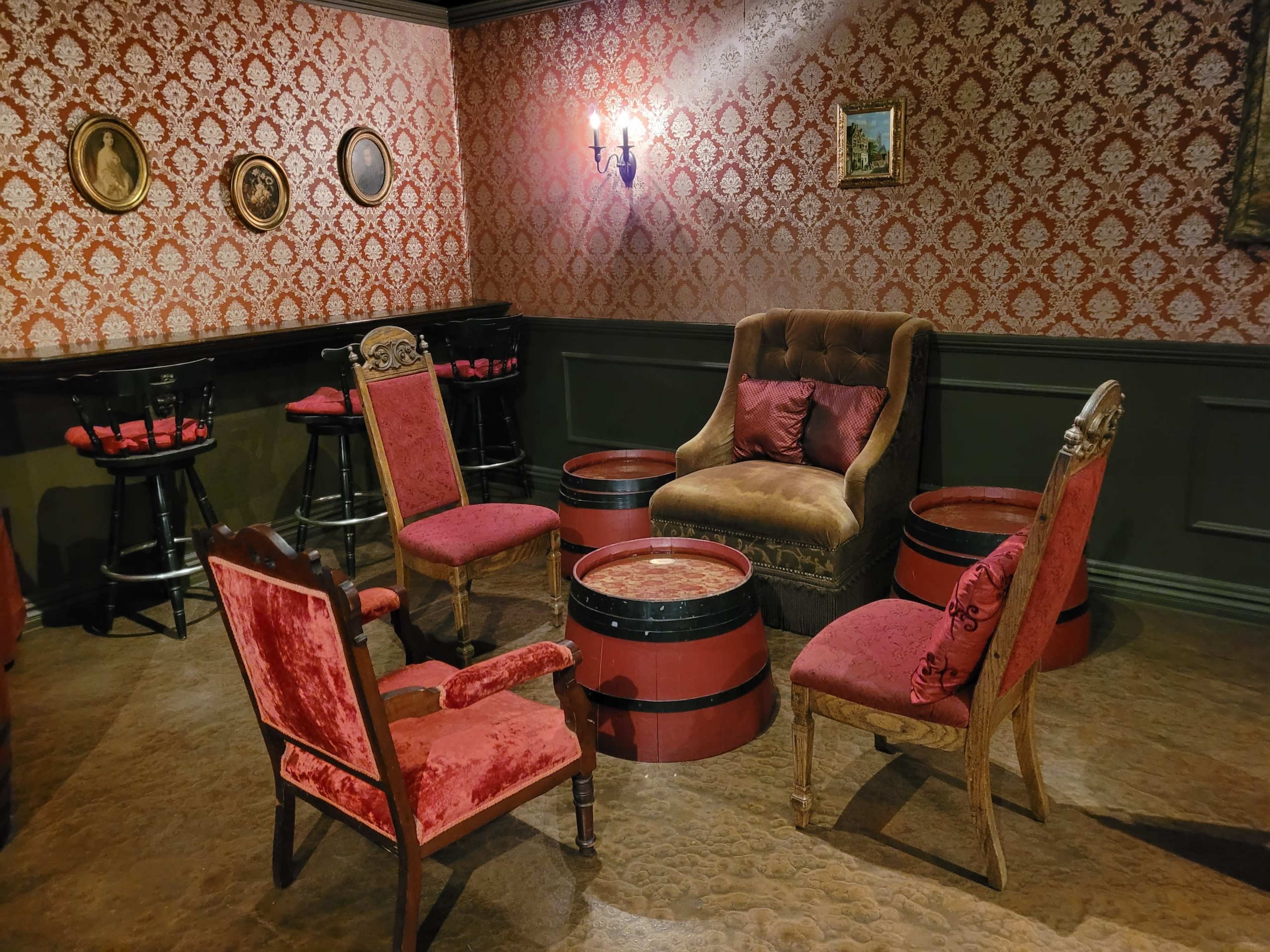 A vintage-style seating area with four chairs and a plush armchair arranged around a circular table, all set against a patterned wallpaper backdrop.