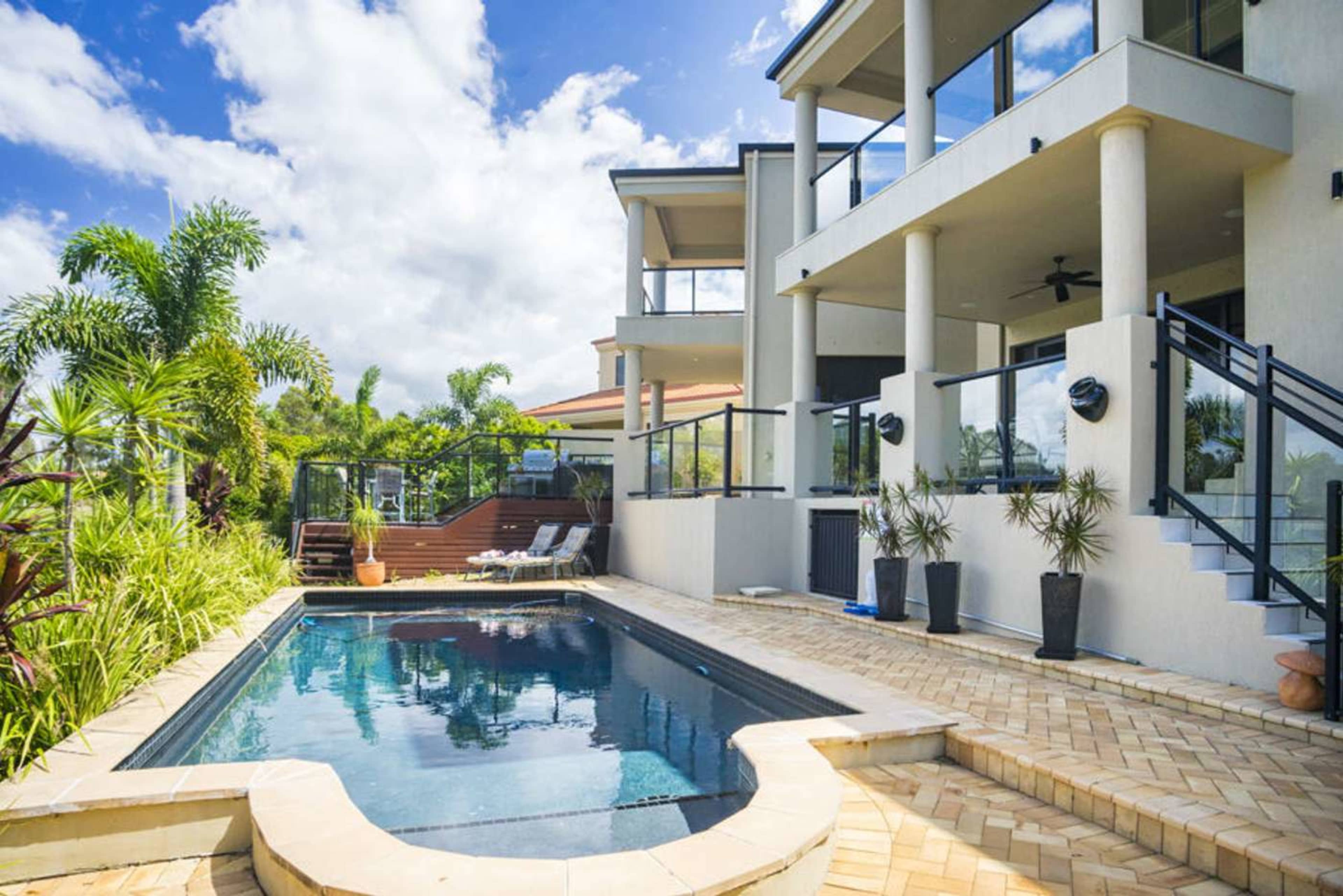 A modern house features a swimming pool surrounded by tropical plants and outdoor seating.