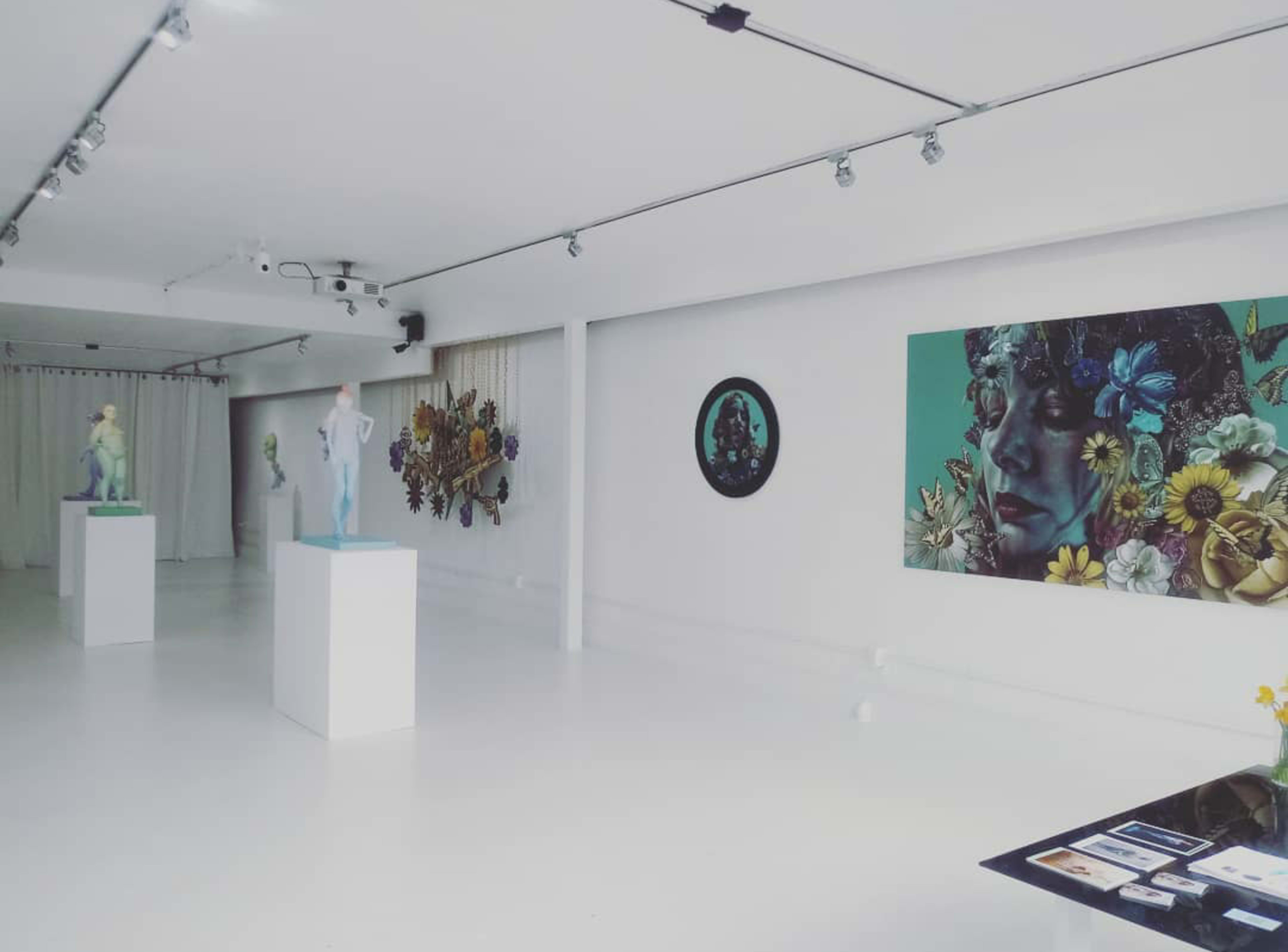 An art gallery featuring sculptures on pedestals and a large mural of a face with floral elements on the wall.