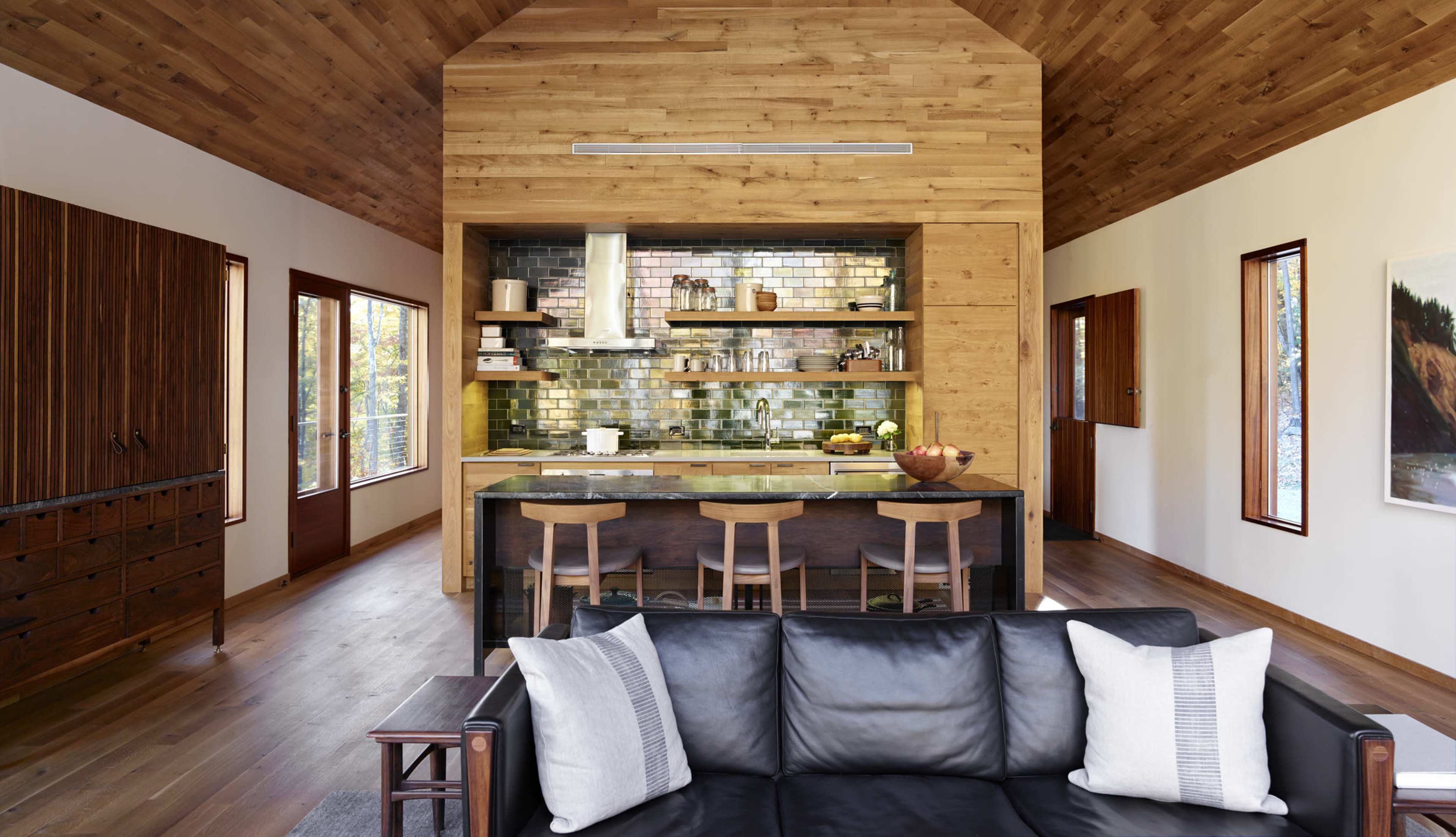 A modern kitchen and living area with wooden walls, a large island with bar stools, and large windows allowing light into the space.