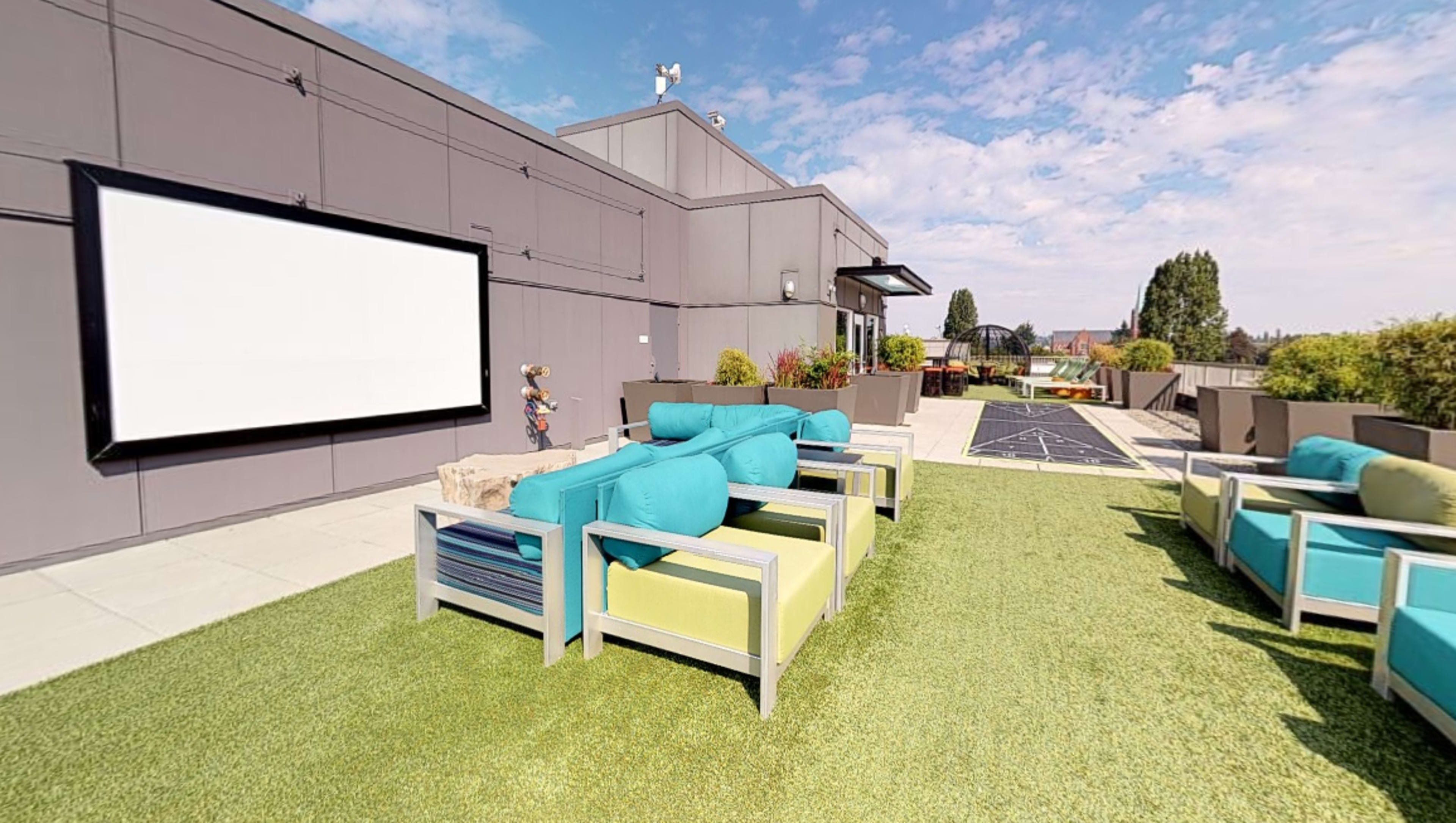 A rooftop patio features colorful seating arrangements and a large screen for outdoor viewing.