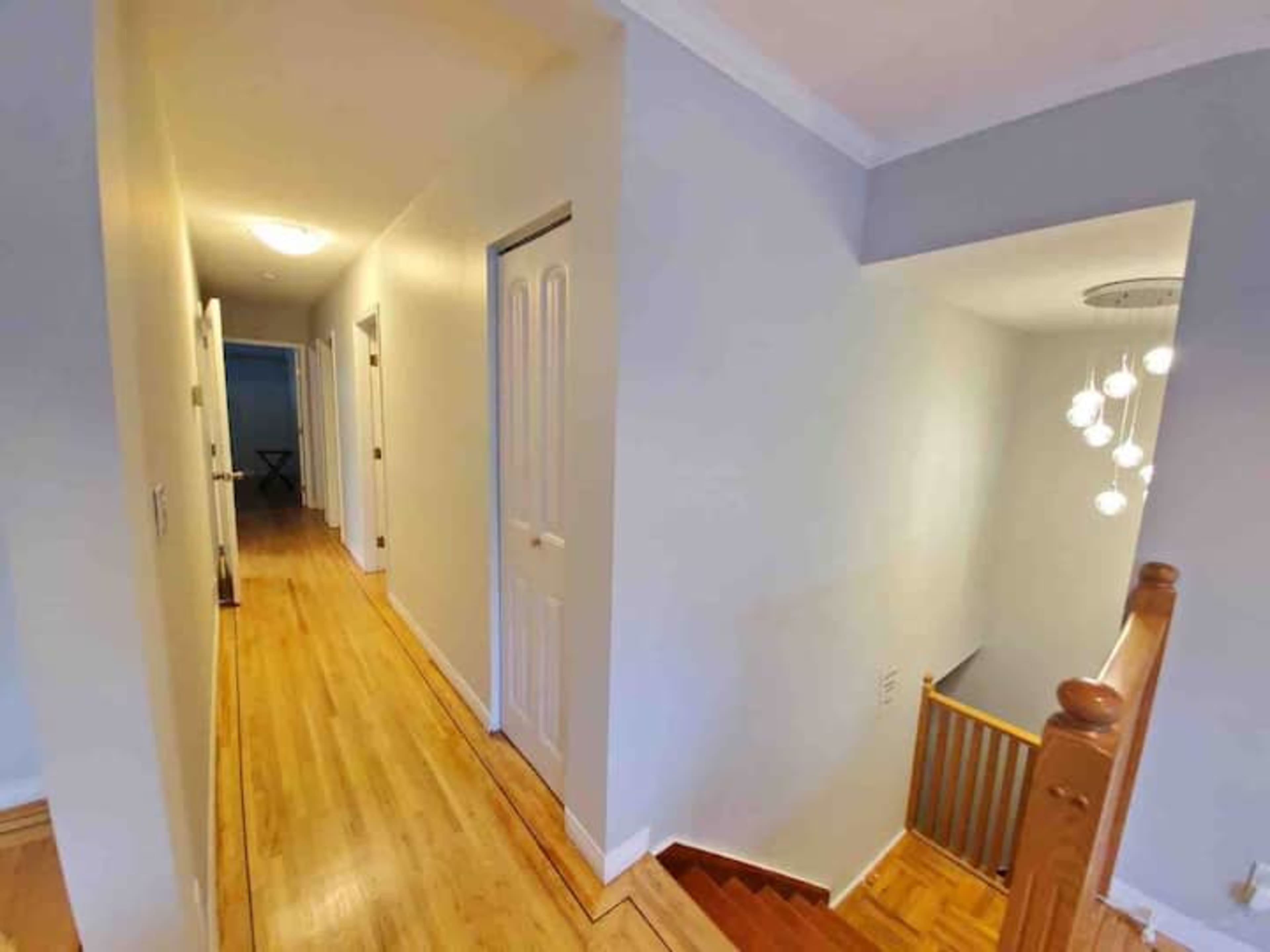 The image shows a hallway with light-colored walls, wooden flooring, and doors leading to different rooms, along with a staircase at the end.