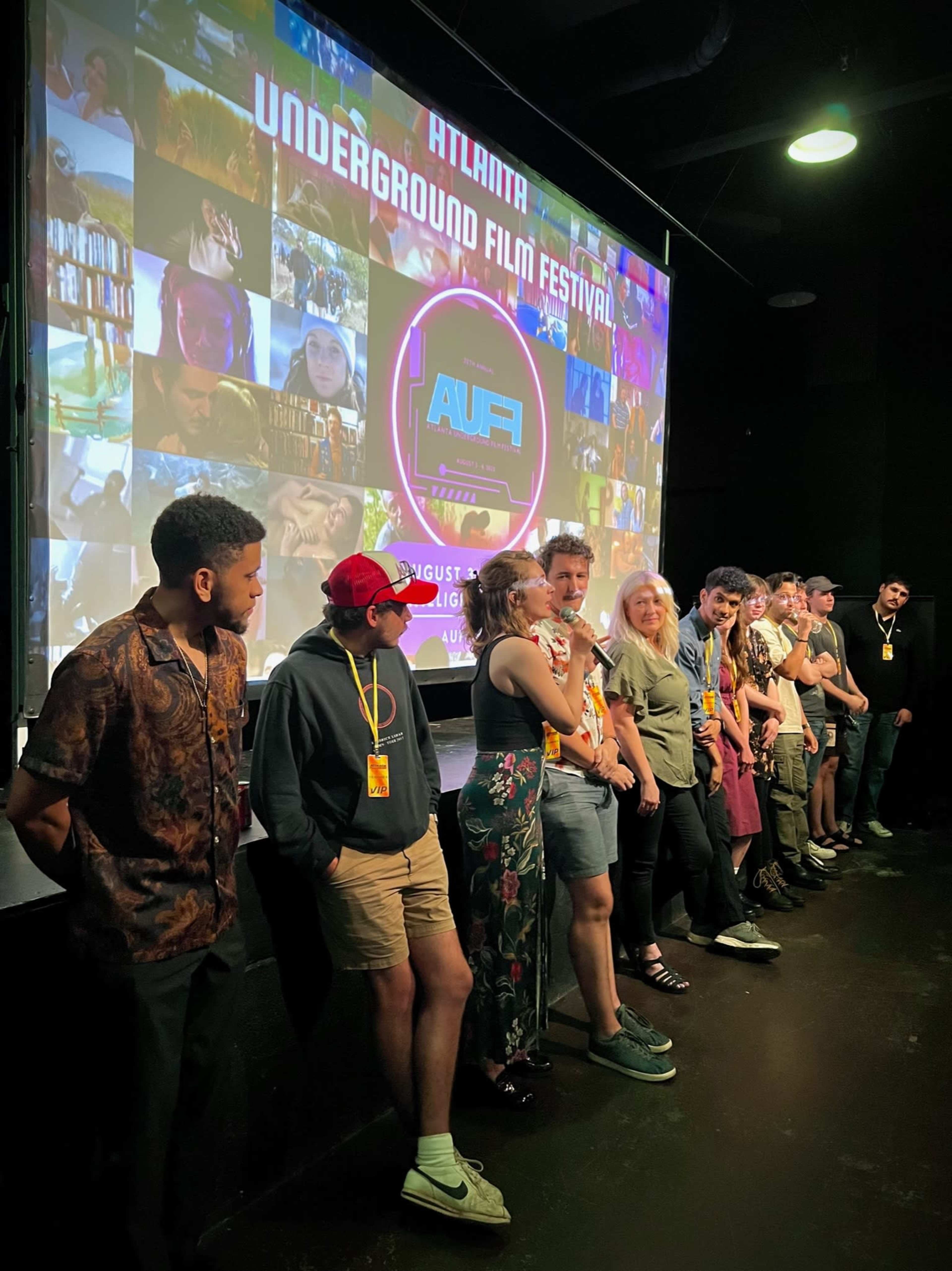 A group of people stands in front of a large screen displaying promotional images for the Atlanta Underground Film Festival.