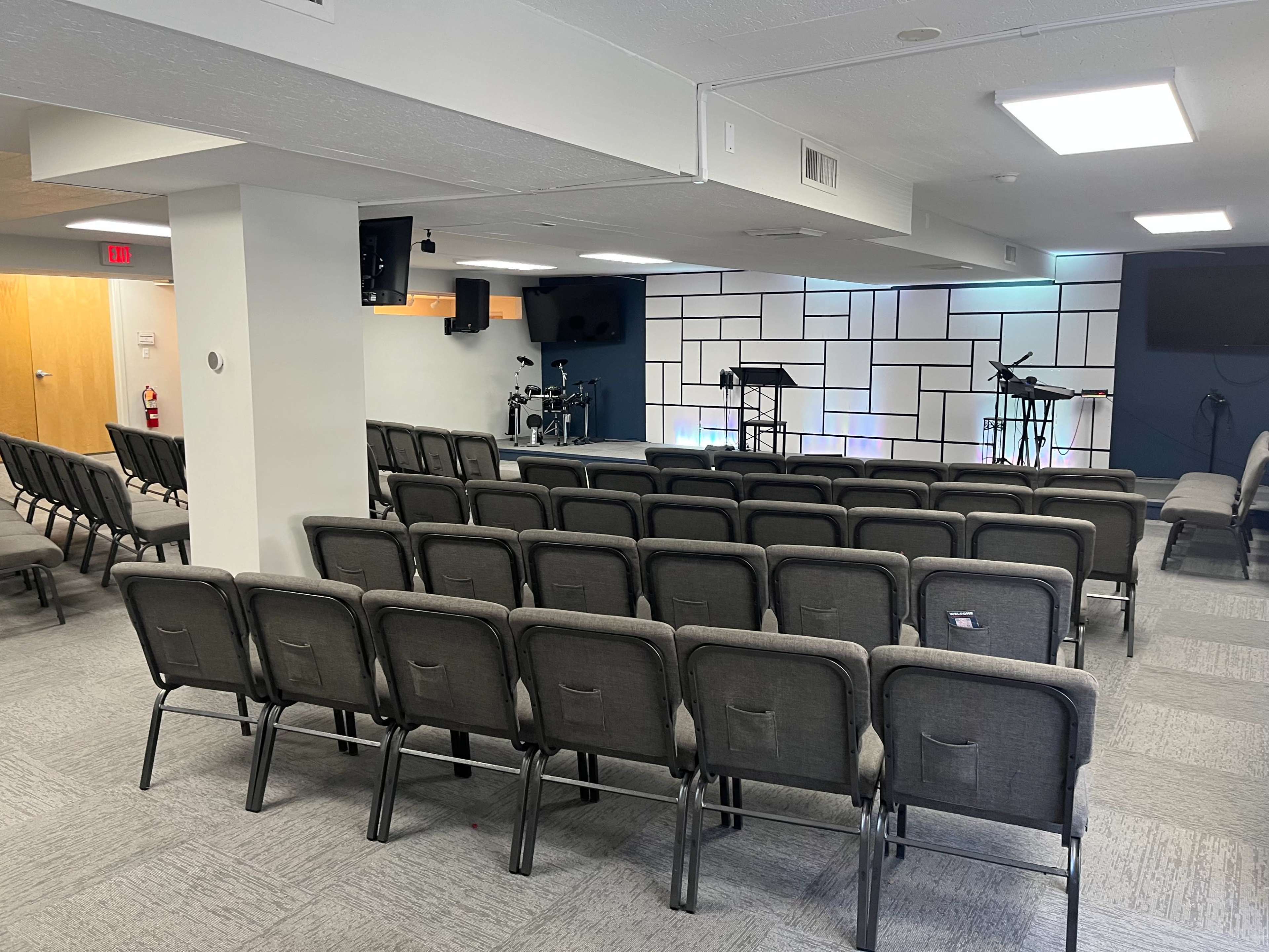 A seating area in a room with rows of gray chairs facing a small stage equipped with microphones and instruments.