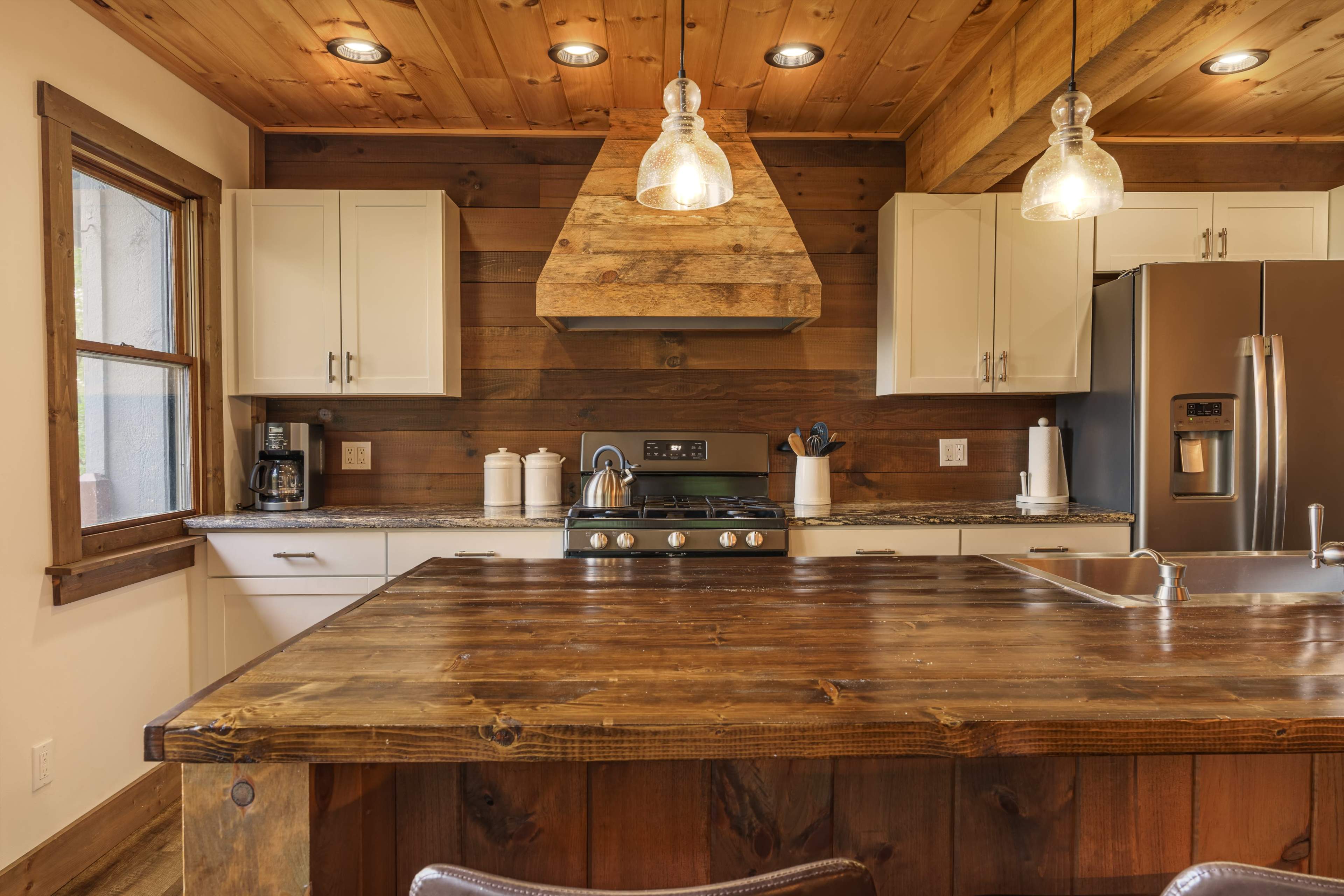 The kitchen features a large wooden island with a gas stove and a stainless steel refrigerator, surrounded by wooden walls and white cabinetry.