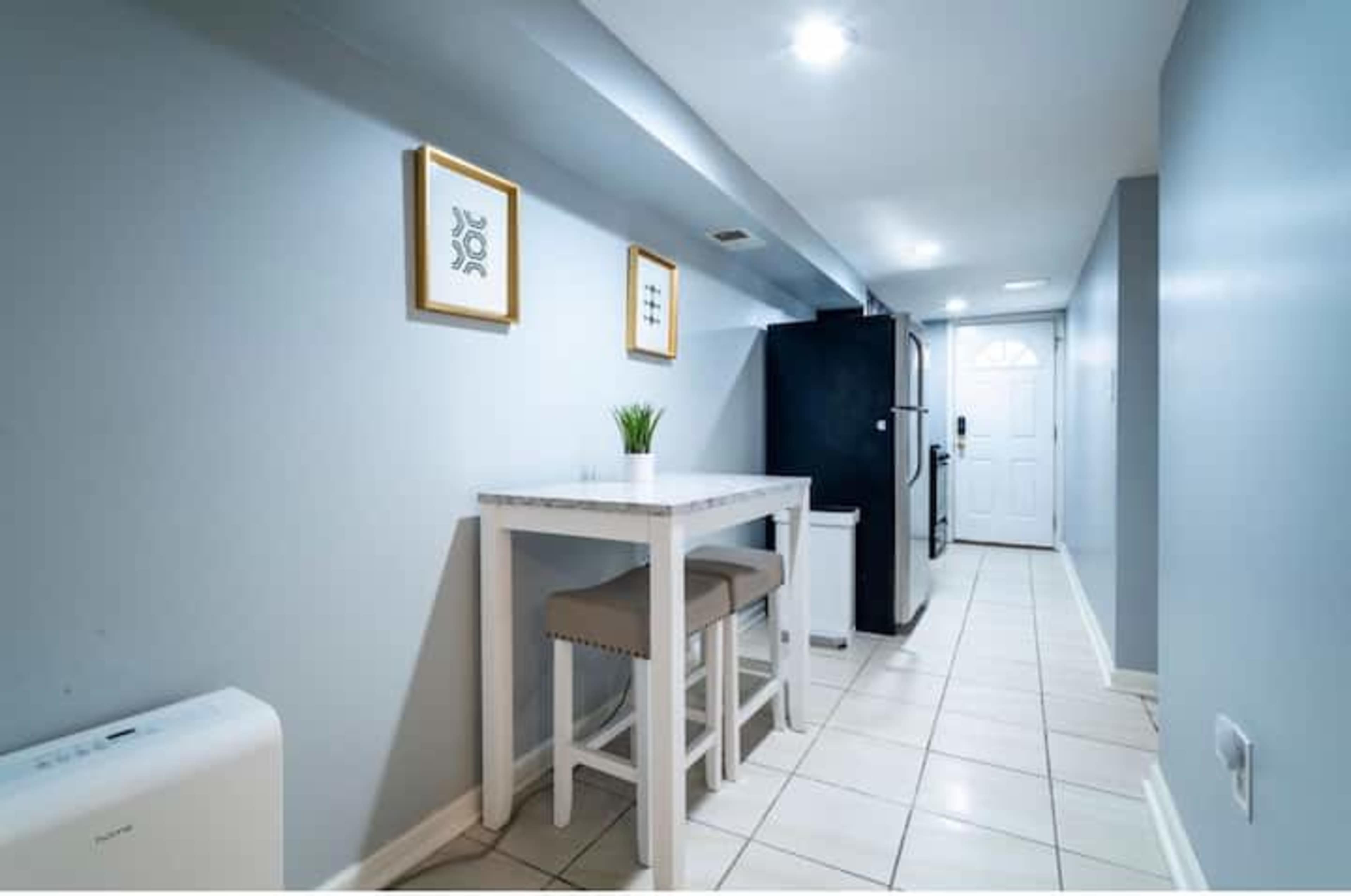 A narrow hallway with a small dining table and two stools, a refrigerator, and a door at the end.