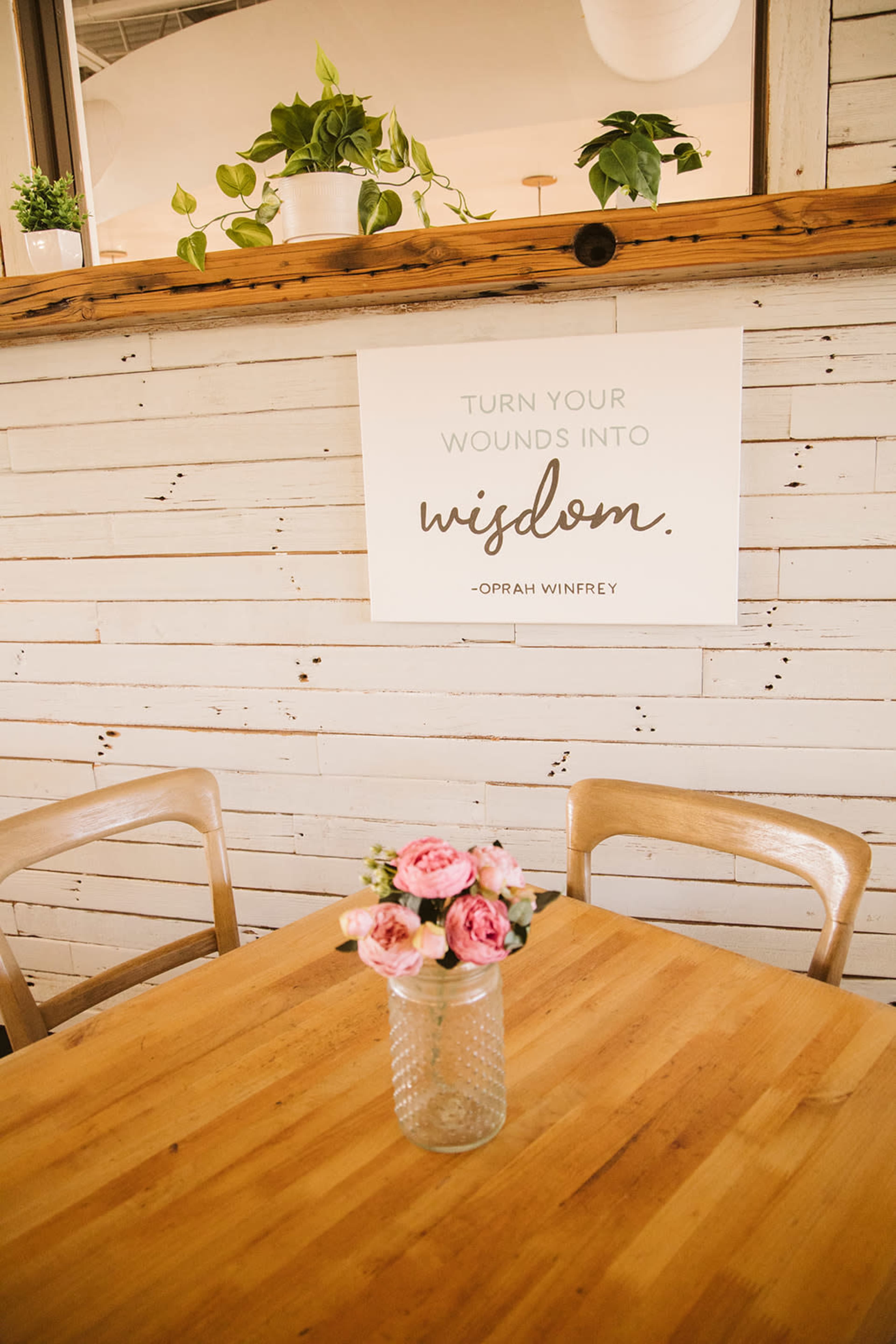 A wooden table is set with a vase of pink flowers, and a sign on the wall above reads, "TURN YOUR WOUNDS INTO wisdom."