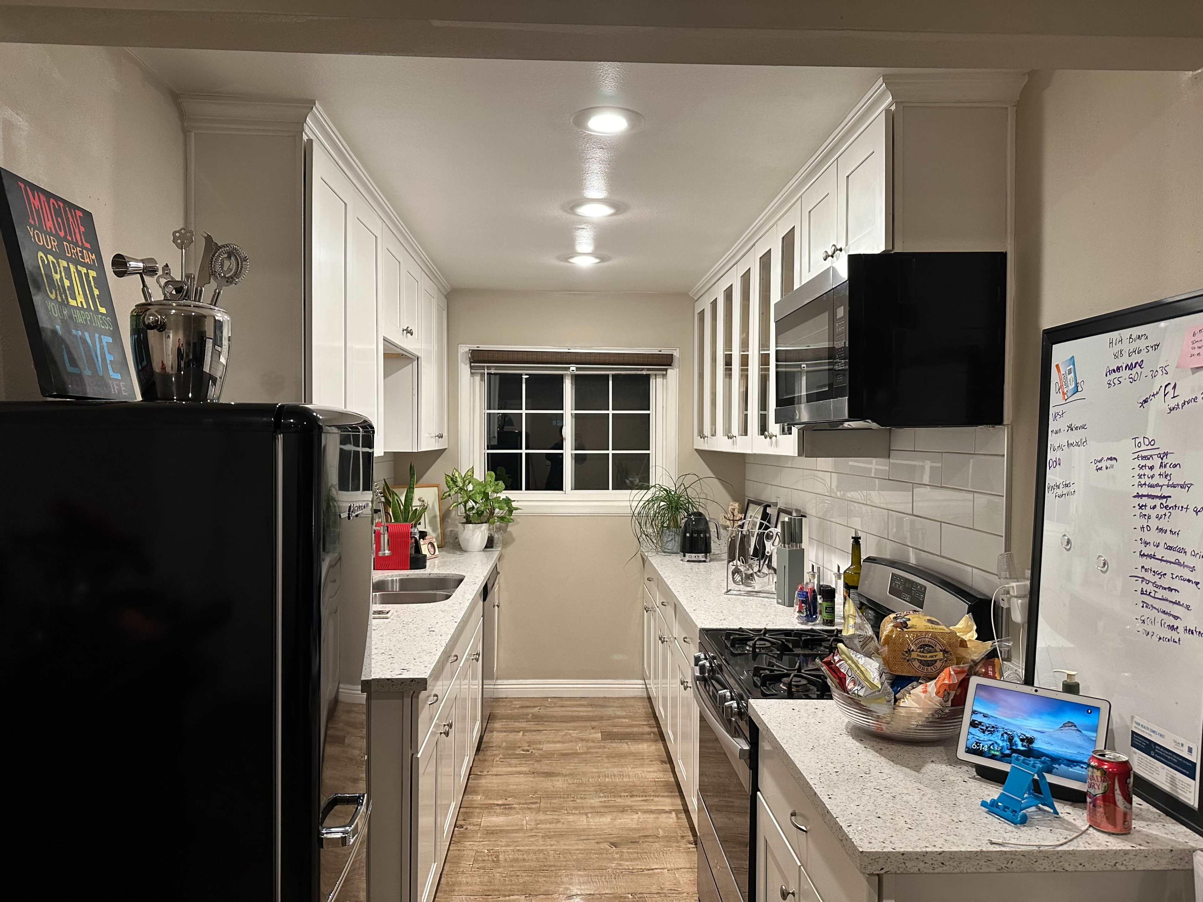 A modern kitchen features white cabinets, stainless steel appliances, and a countertop lined with snacks and a tablet.