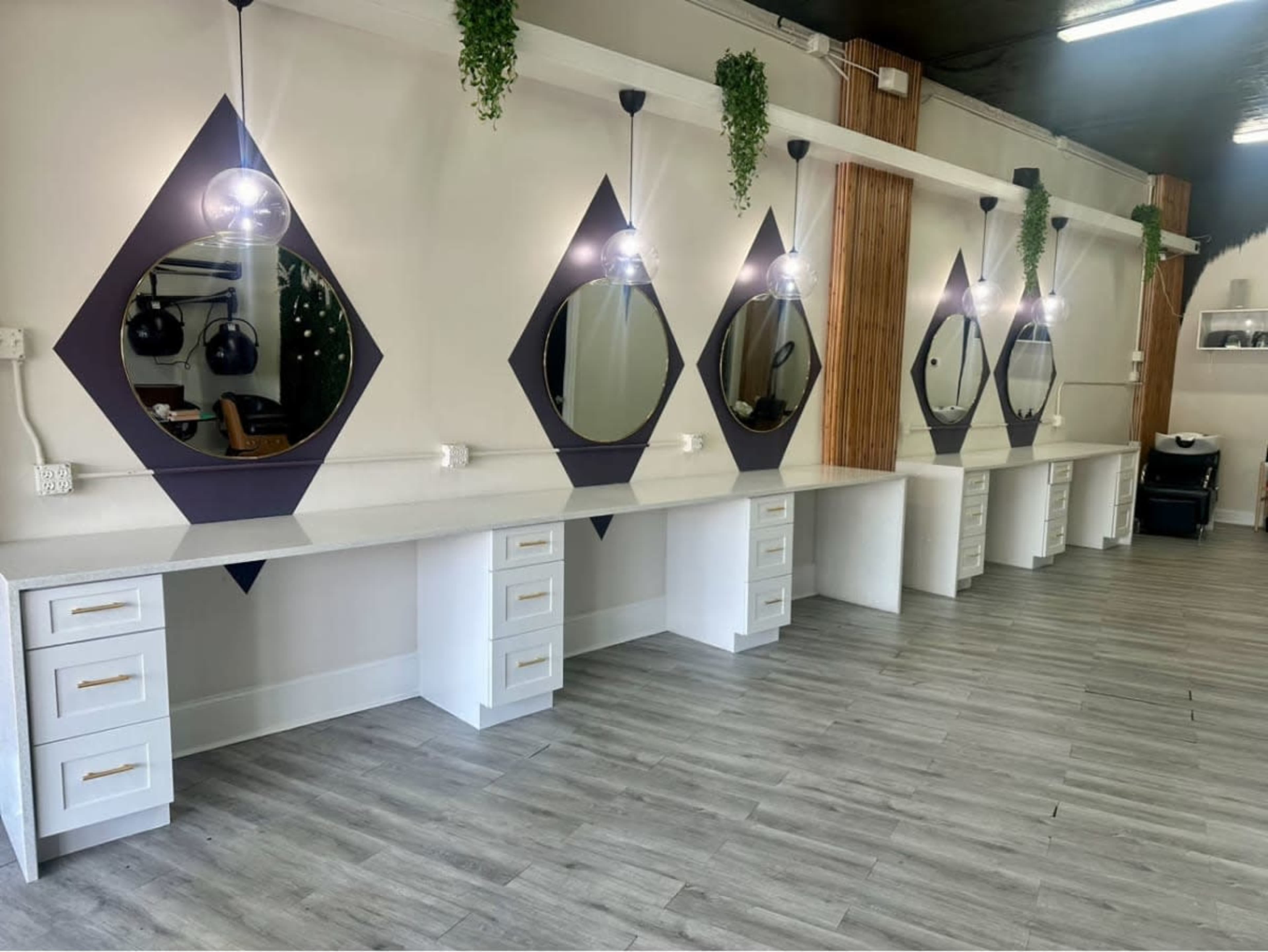 The image shows a well-lit salon with multiple white vanities featuring diamond-shaped mirrors, each accompanied by small potted plants above.