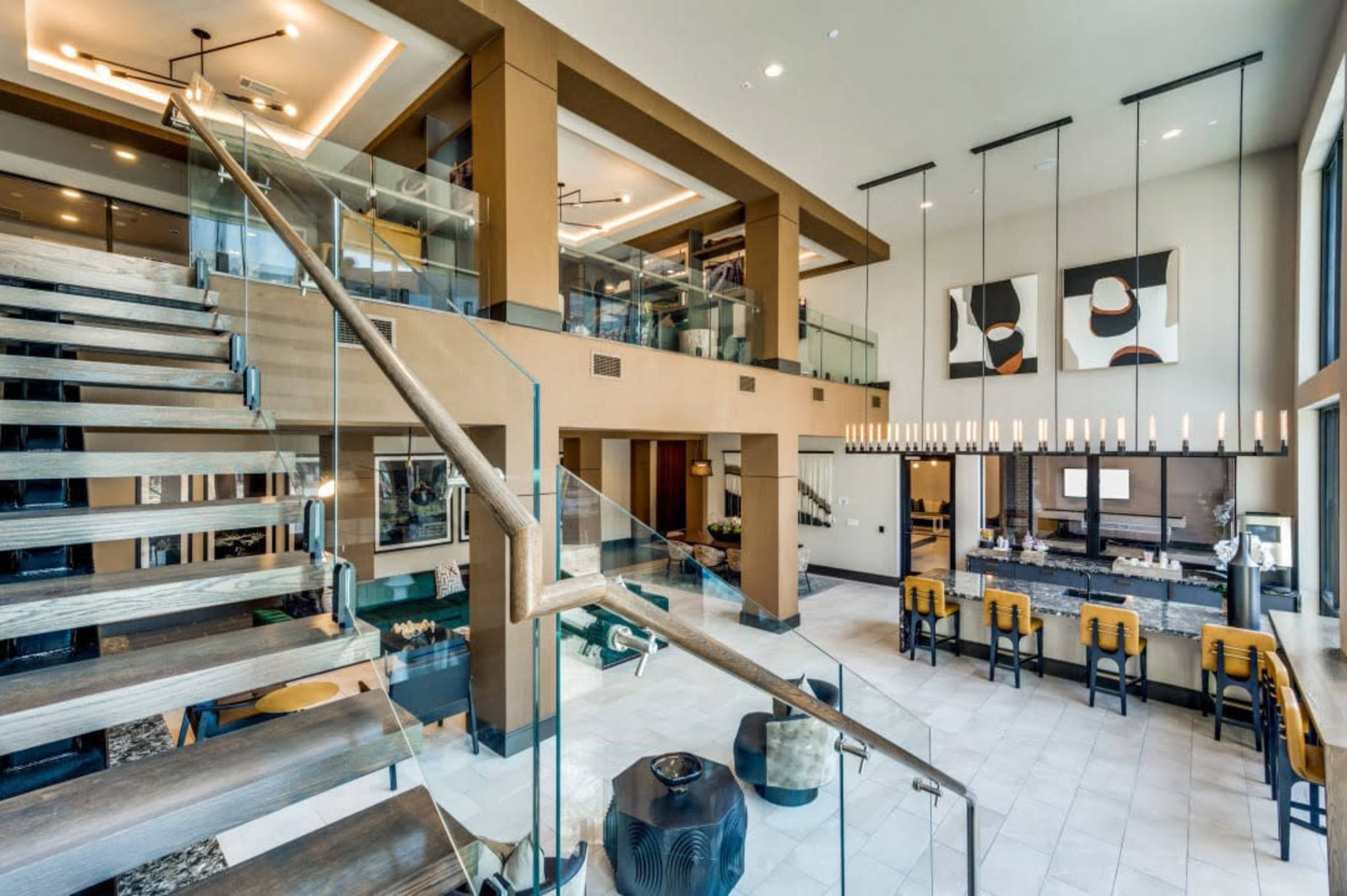 A modern, multi-level interior space featuring a staircase leading to an upper area, with a bar and a lounge area visible in the background.