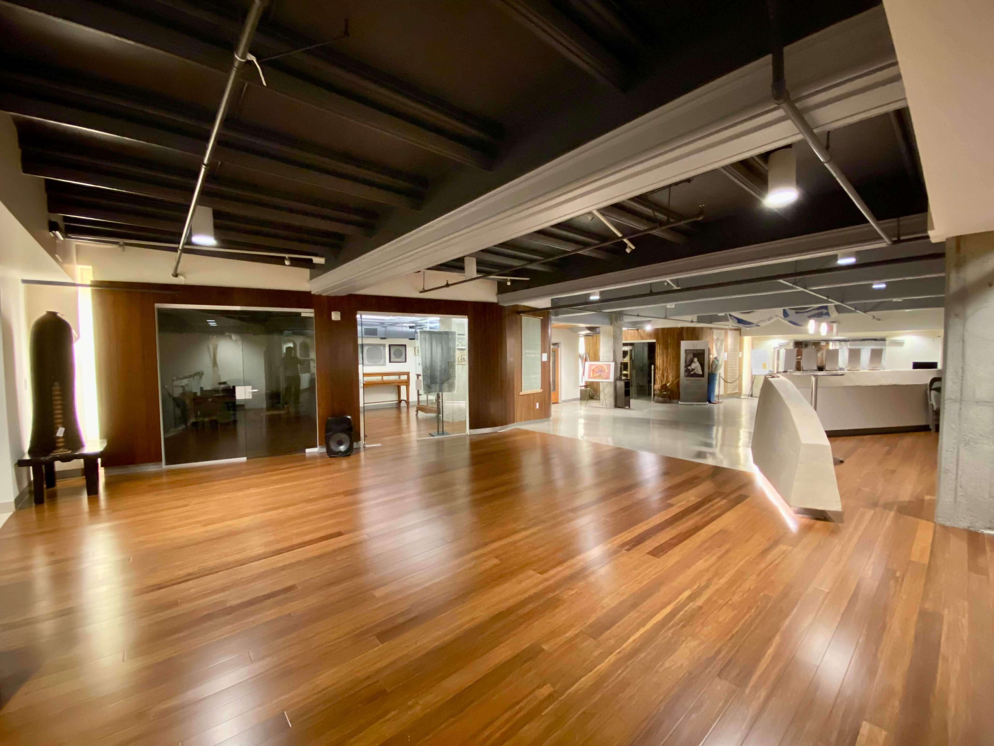 The image shows a spacious, modern interior with polished wooden floors, exposed beams, and various art pieces displayed on the walls.