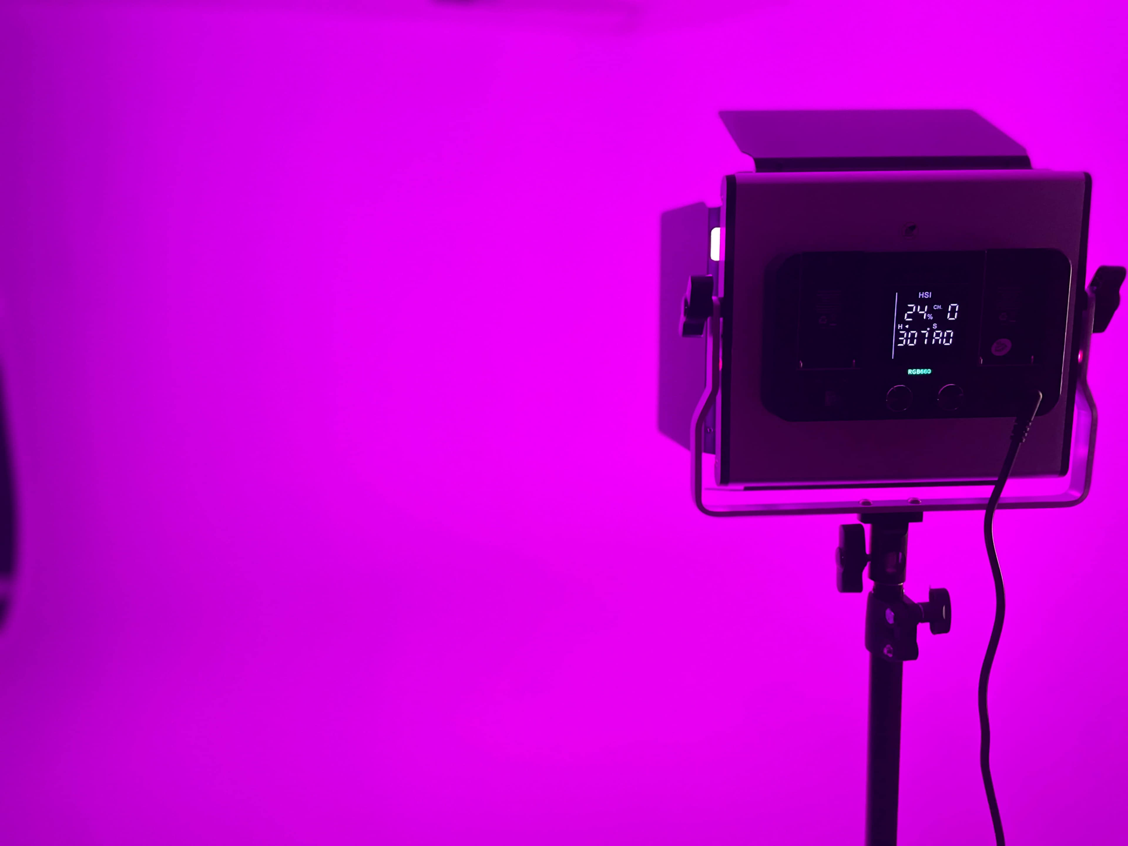 A lighting panel on a stand emits purple light against a plain backdrop.
