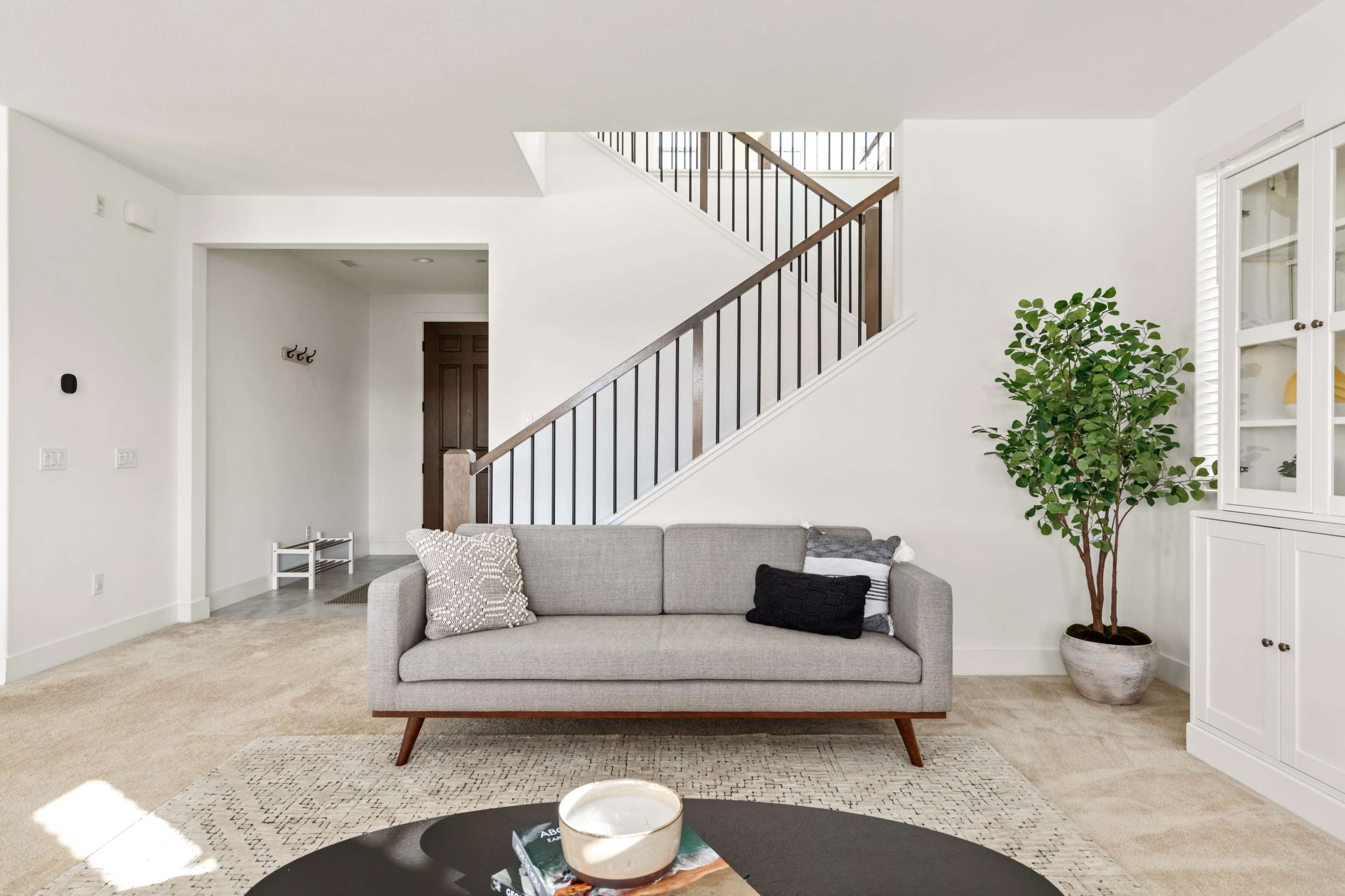 A modern living room featuring a gray sofa, a round coffee table, a potted plant, and a staircase in the background.
