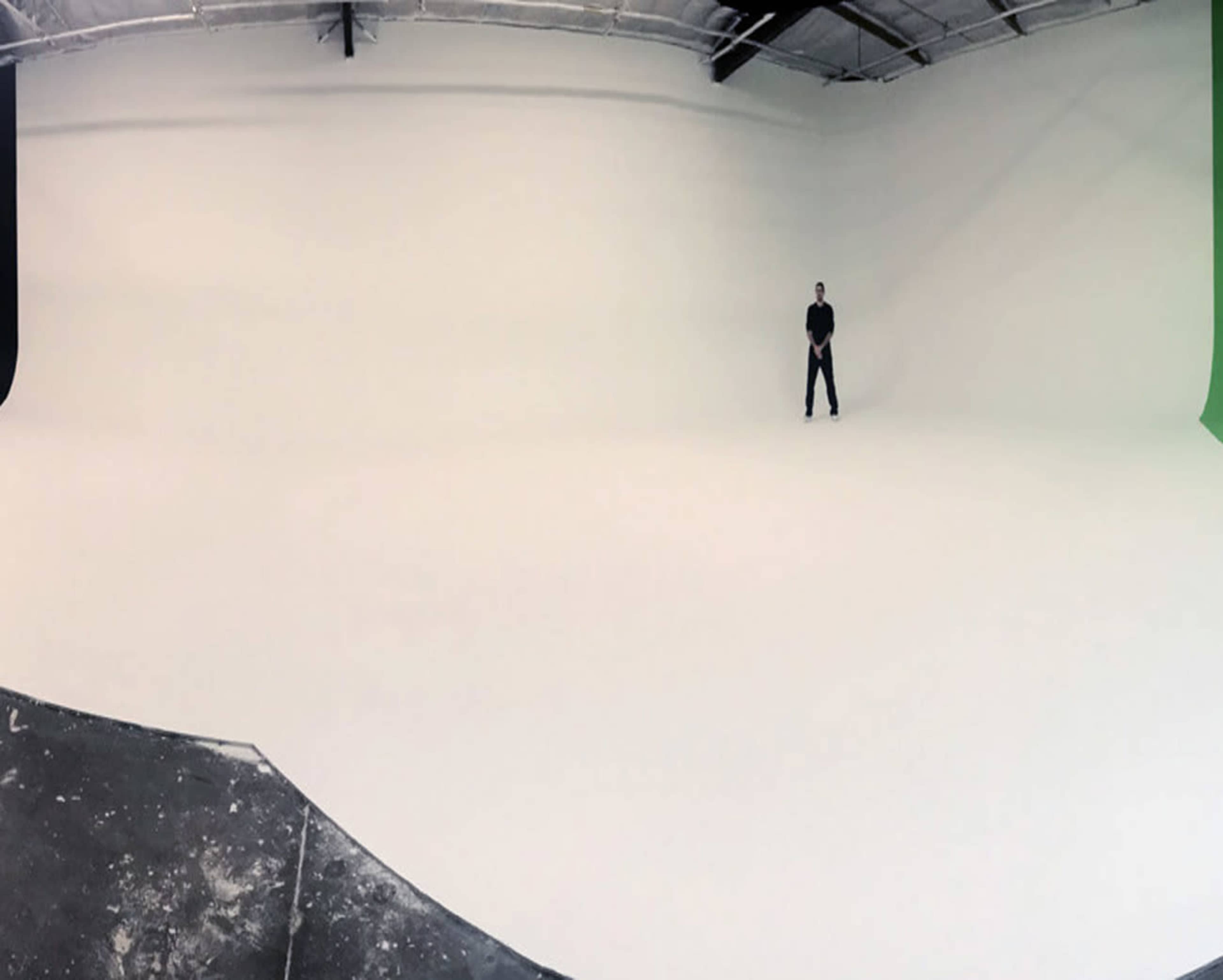 A person stands alone in a spacious, empty photography studio with a smooth white backdrop.