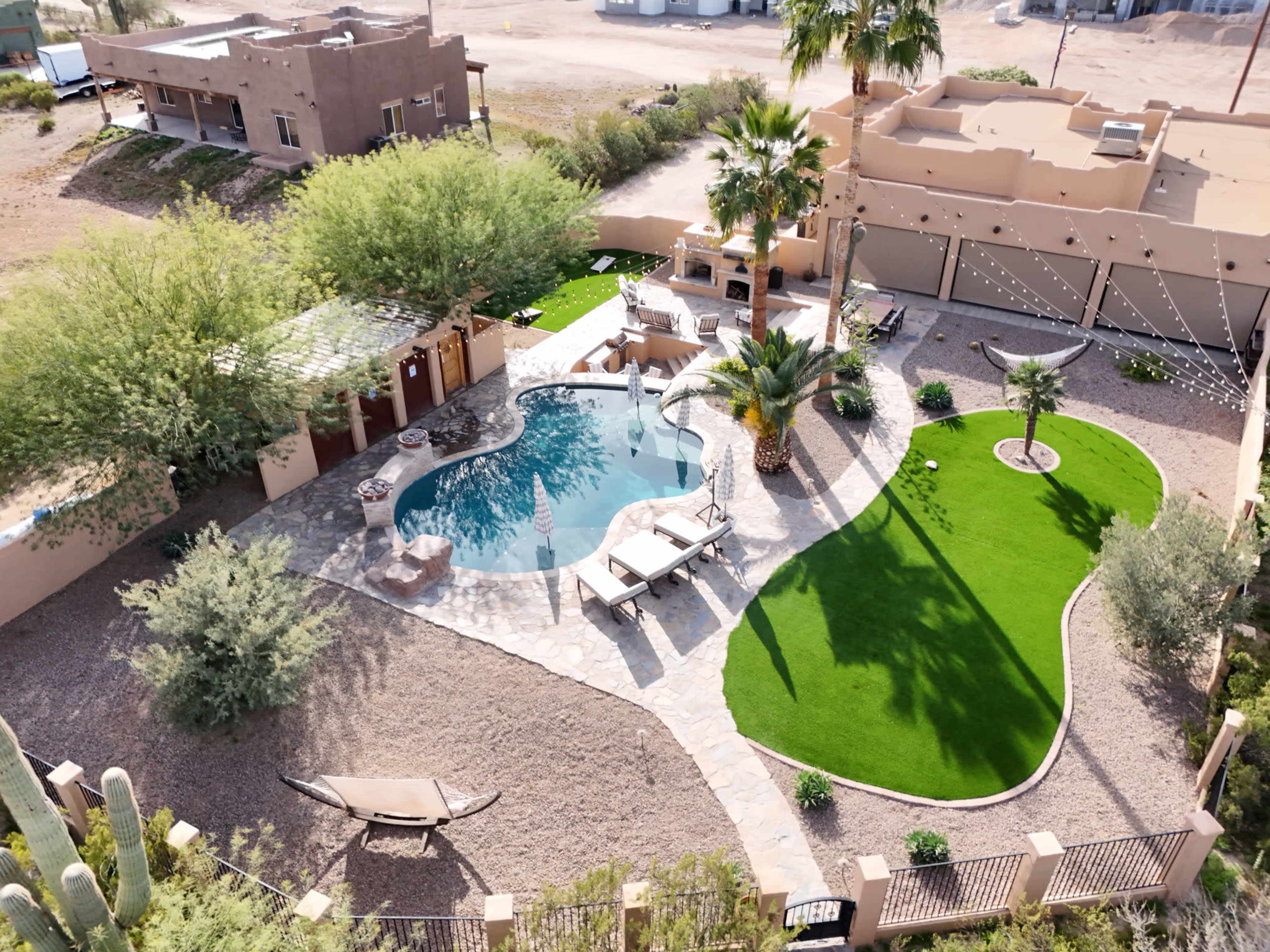 The image shows a landscaped backyard with a swimming pool, palm trees, and a small lawn area surrounded by gravel.