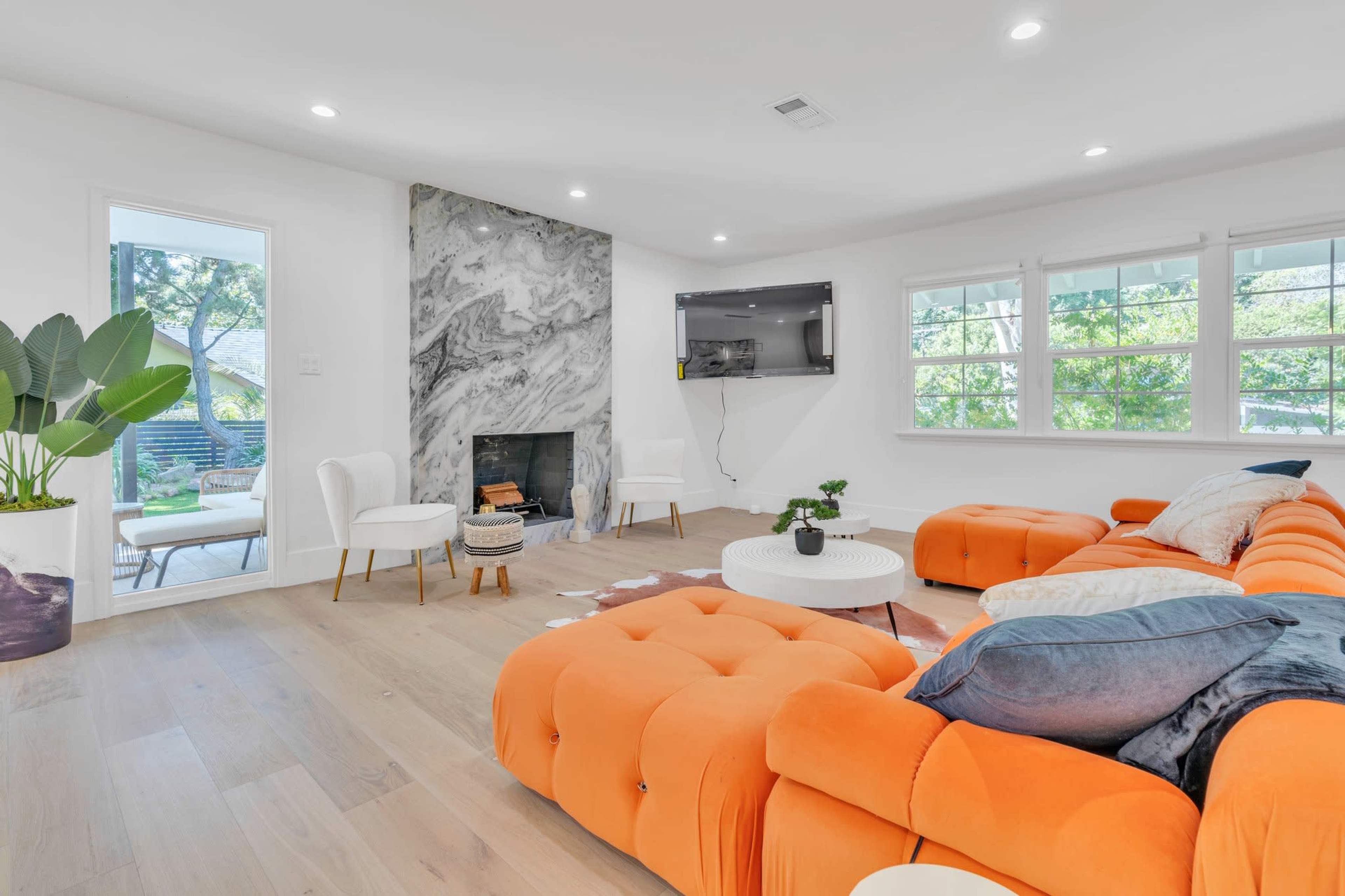 The living room features an orange sectional sofa, a white coffee table, and a marble accent wall with a fireplace.