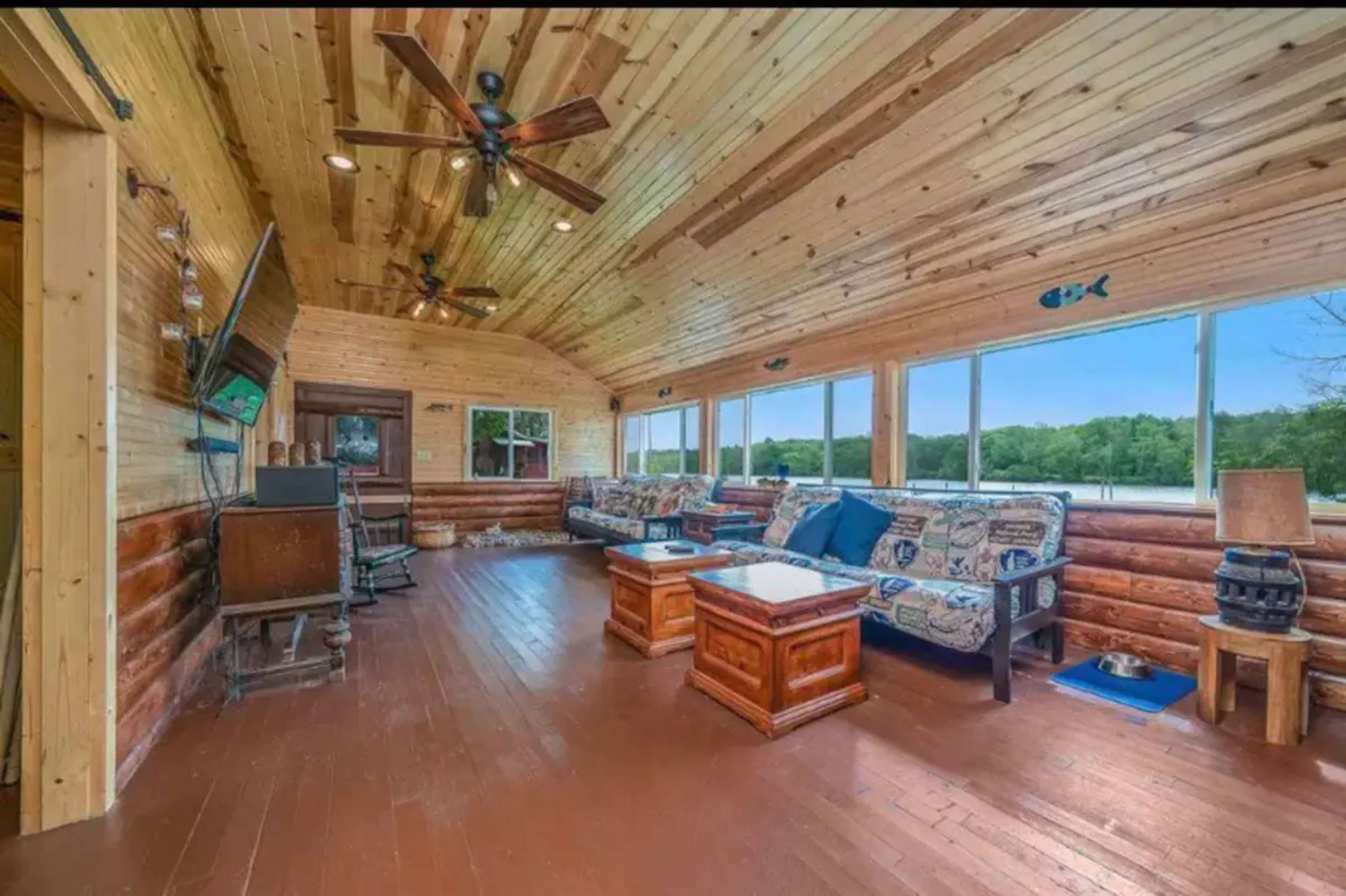 A wooden sunroom furnished with sofas, a coffee table, and large windows overlooking a green landscape.