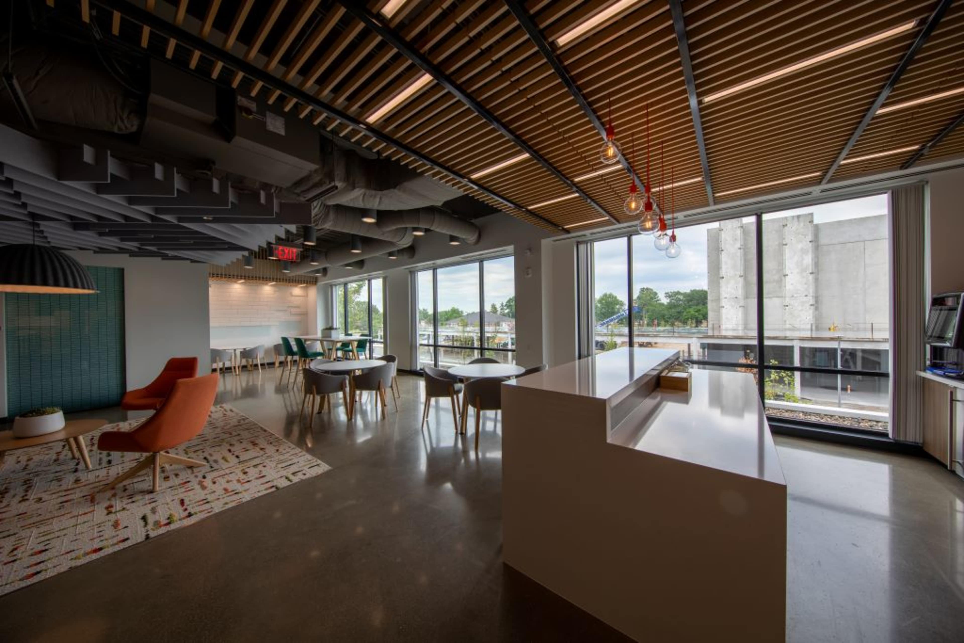 The image shows a modern office interior featuring a reception area with a white counter, colorful seating, and large windows overlooking a construction site.