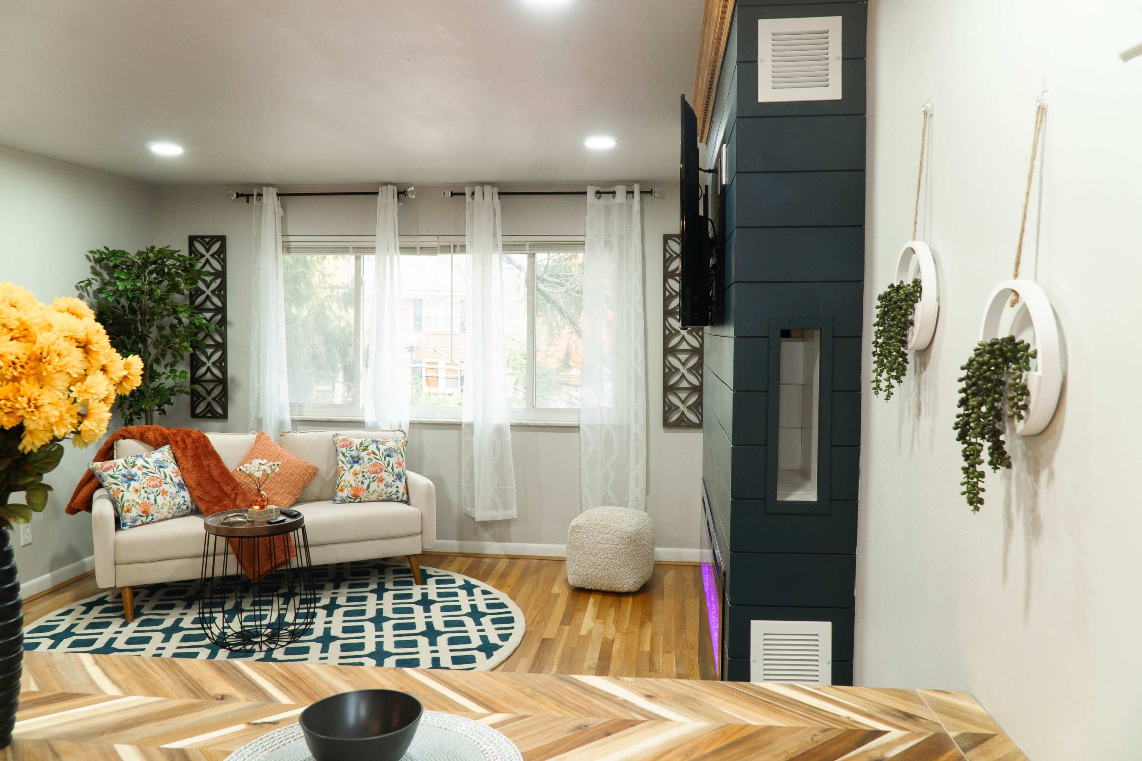 The living room features a light-colored sofa with decorative pillows, a round area rug, and a mounted television against a dark accent wall.