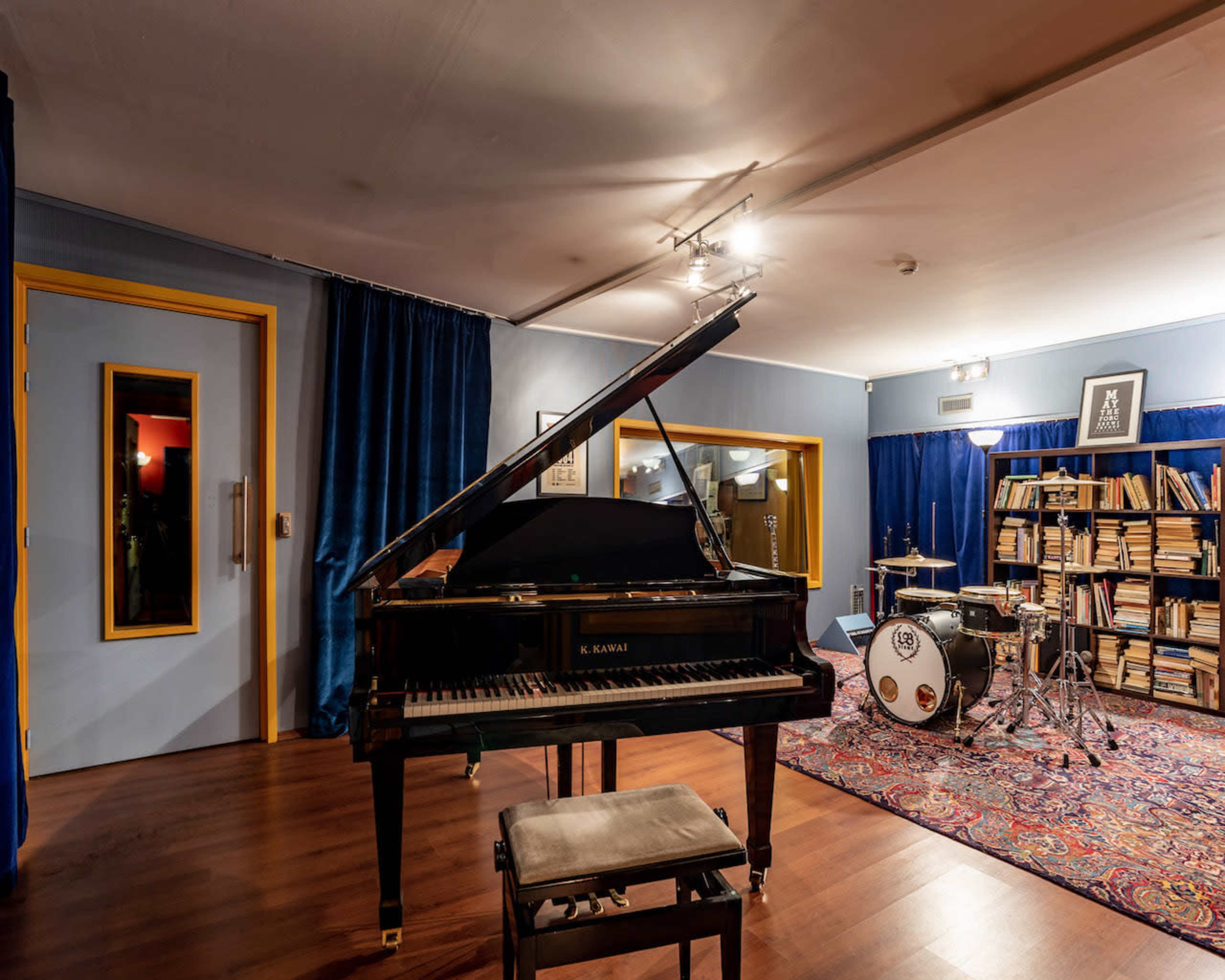 A music studio featuring a grand piano, a drum set, and shelves filled with books.