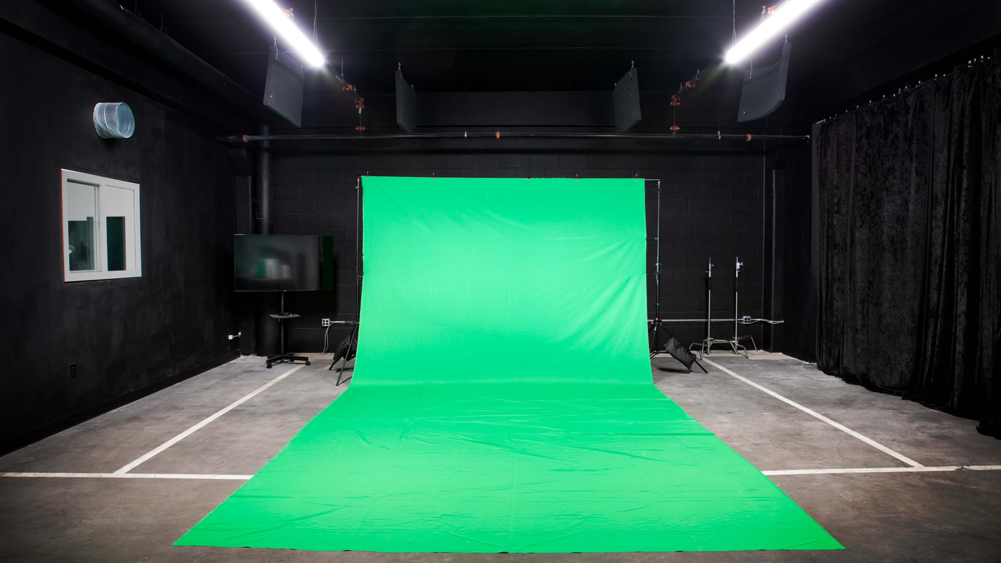 An empty studio space featuring a green backdrop, floor, and minimal equipment in a dimly lit environment.