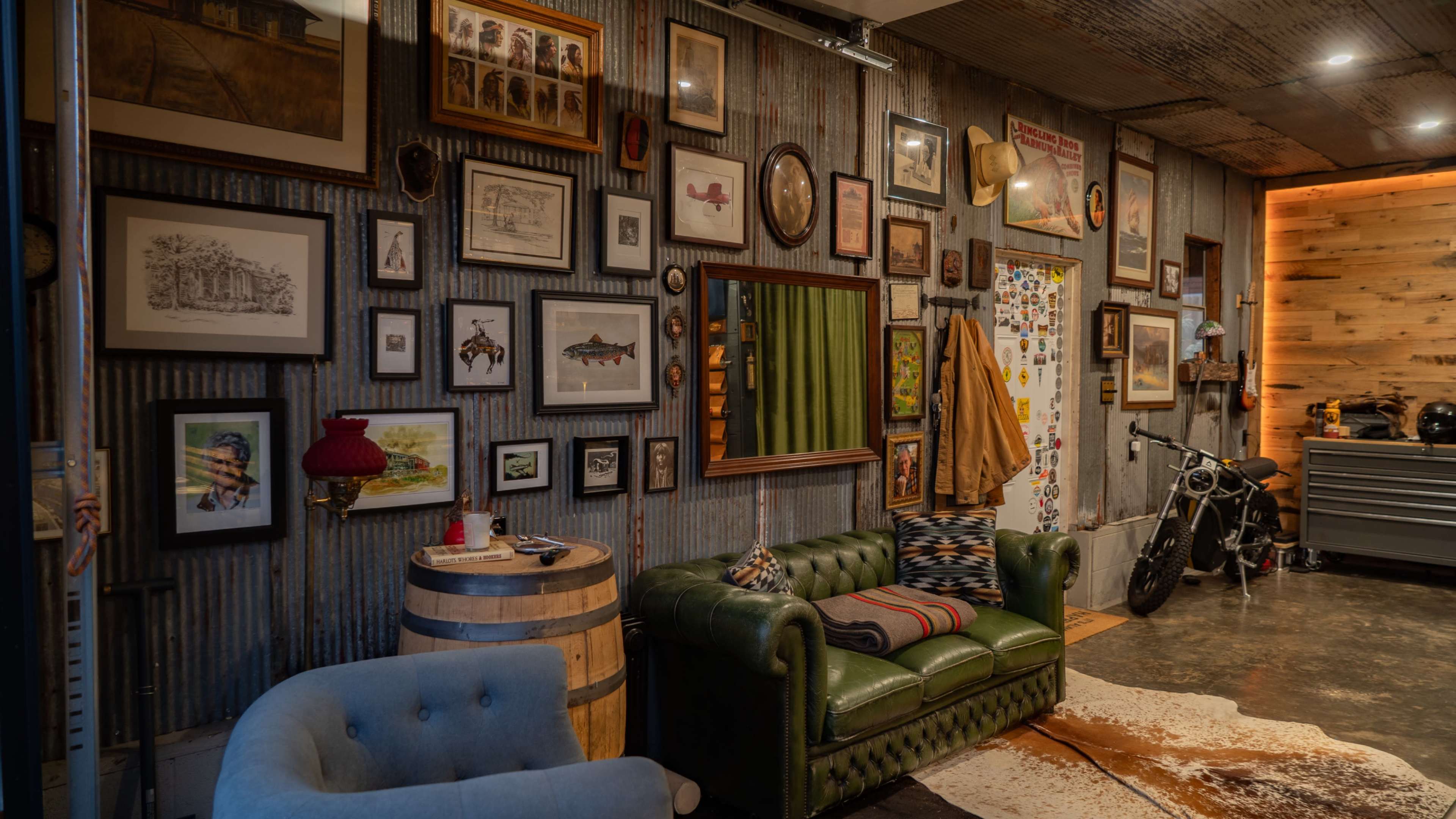 The image depicts a cozy, eclectic room featuring a green leather sofa, a barrel table, and a wall adorned with various framed pictures and decorations.