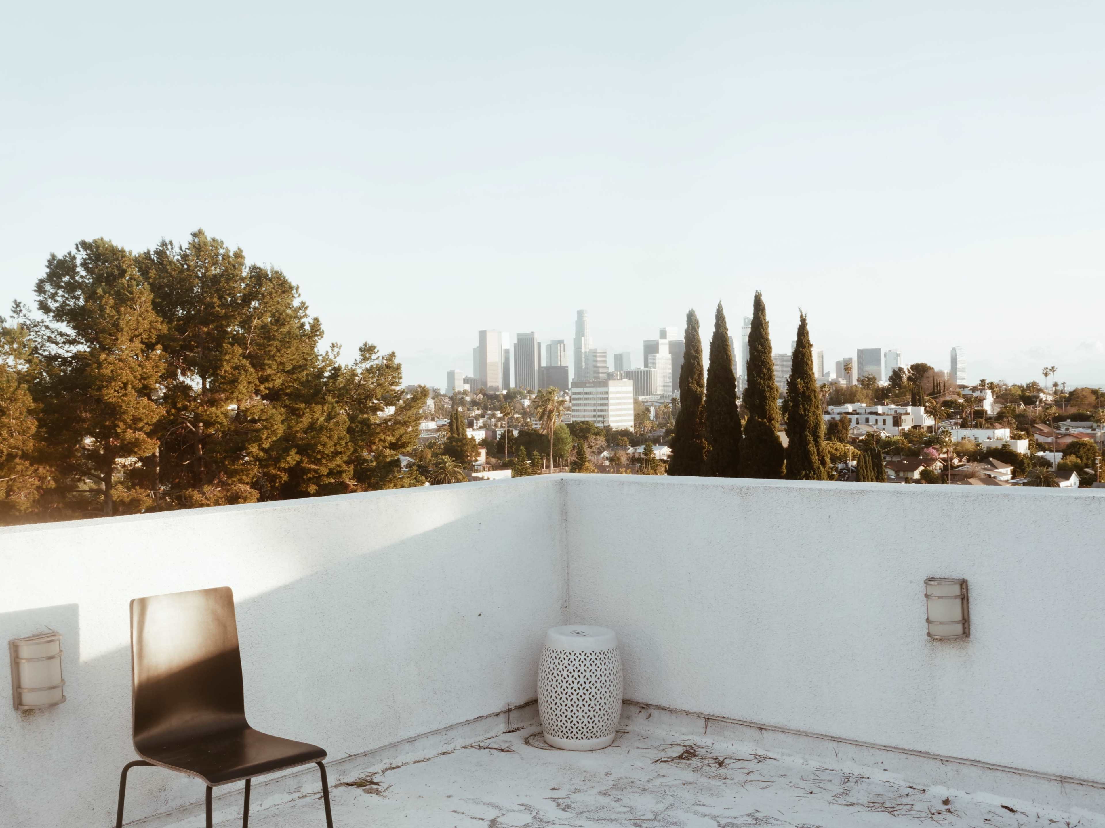 A black chair and a decorative stool sit on a rooftop terrace overlooking the Los Angeles skyline.