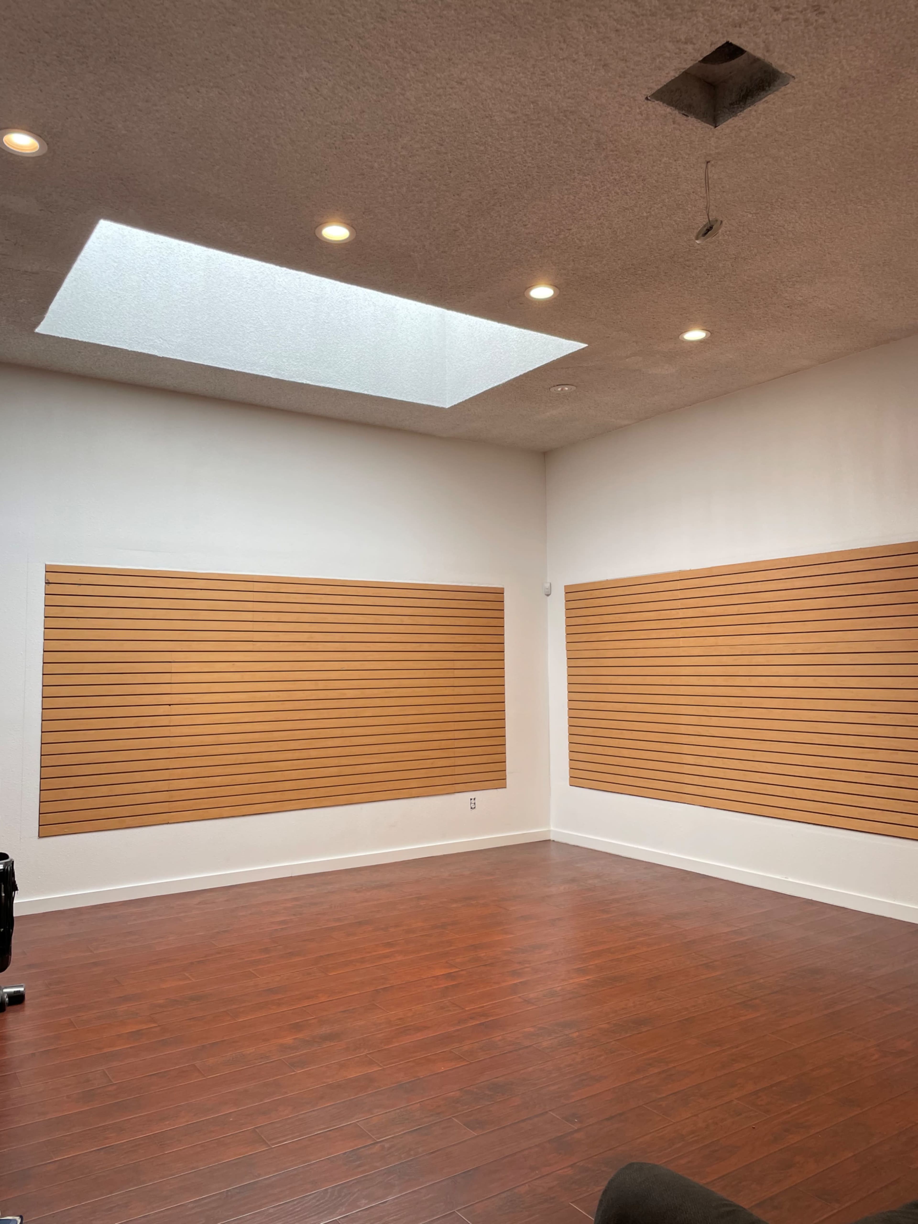 An empty room with wooden slat wall panels and a skylight above, illuminated by recessed lighting.