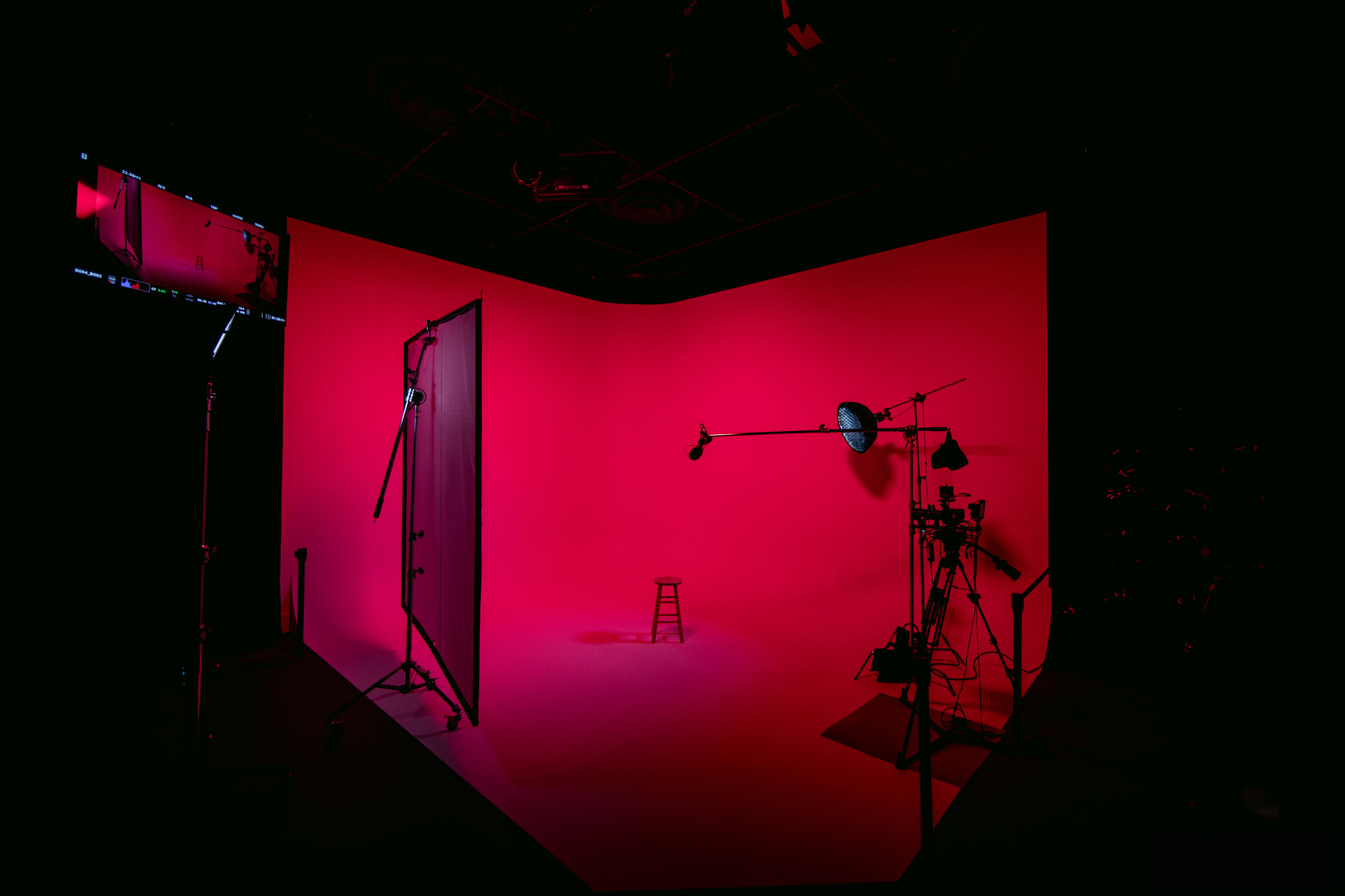A photography studio with a single stool positioned in front of a bright pink backdrop, surrounded by lighting equipment.