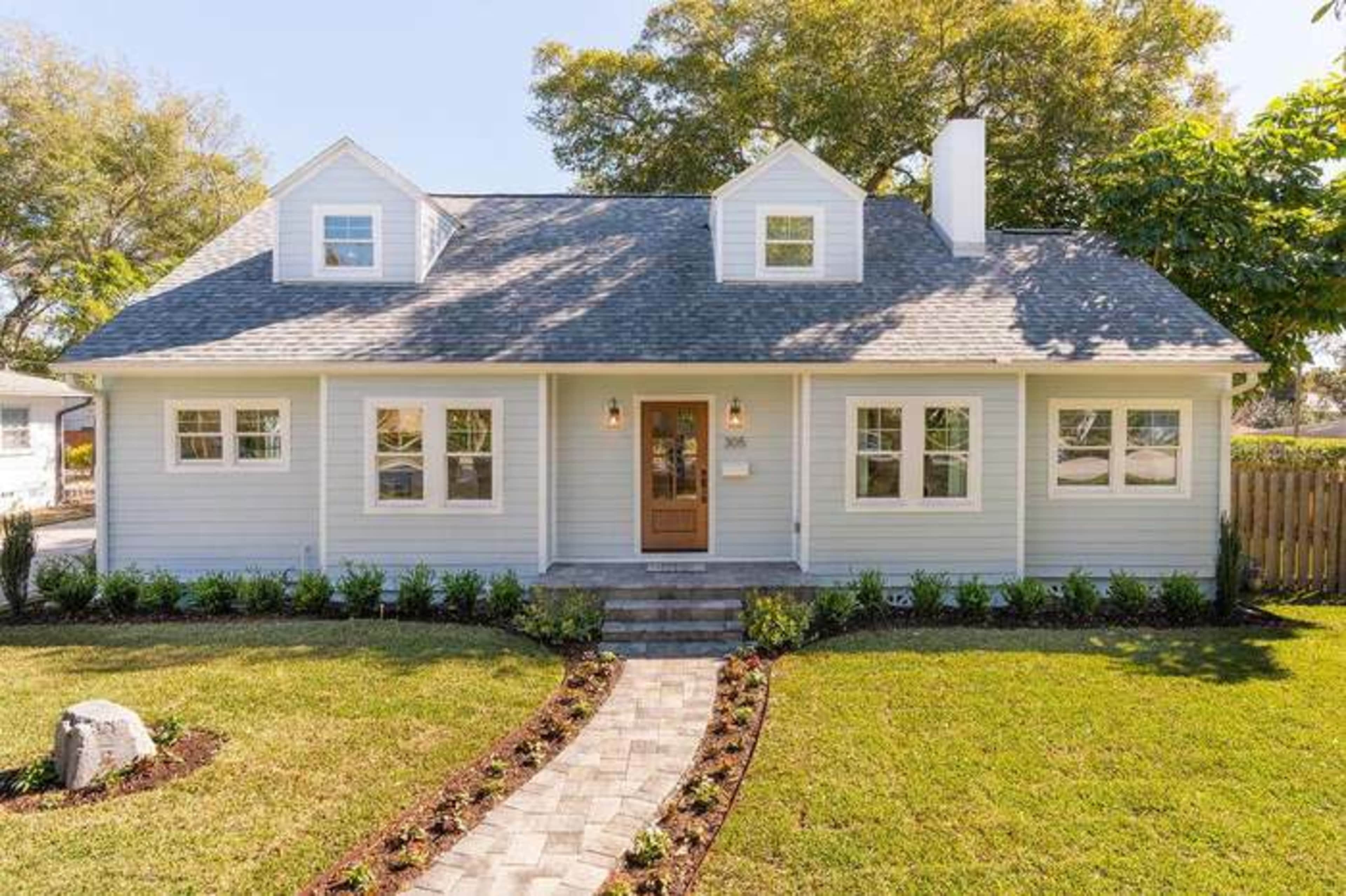 A light blue, one-and-a-half-story house with a front porch and a landscaped garden path leading up to the entrance.