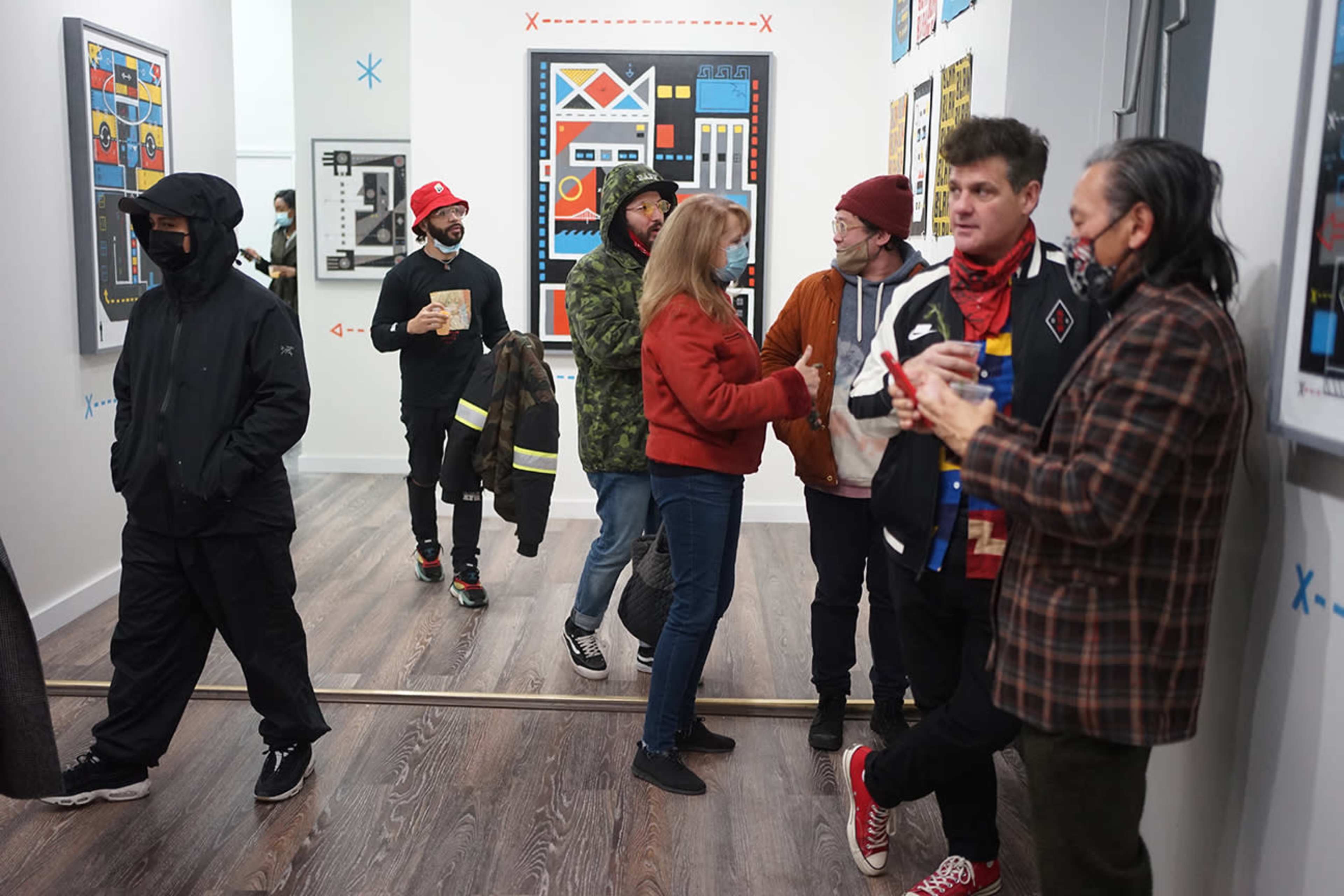 A group of people is interacting and viewing artwork in a gallery space with colorful framed pieces on the walls.