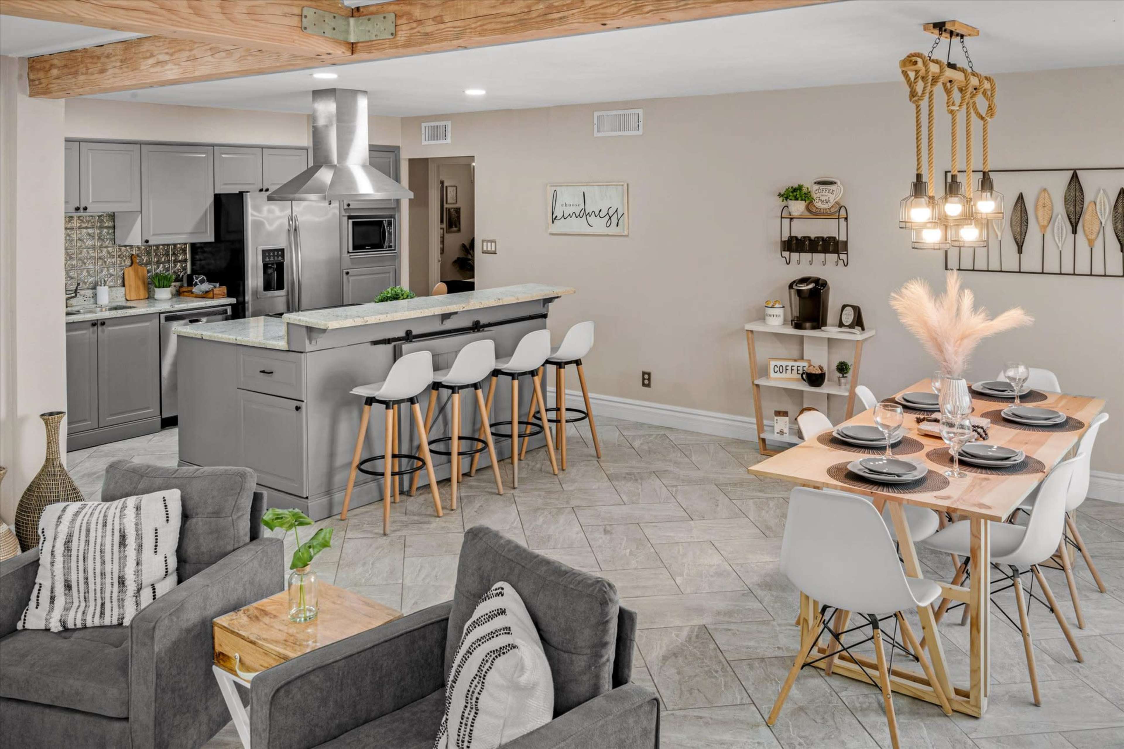 A modern open-concept kitchen and dining area featuring gray cabinets, a large island with seating, and a wooden dining table set for four.