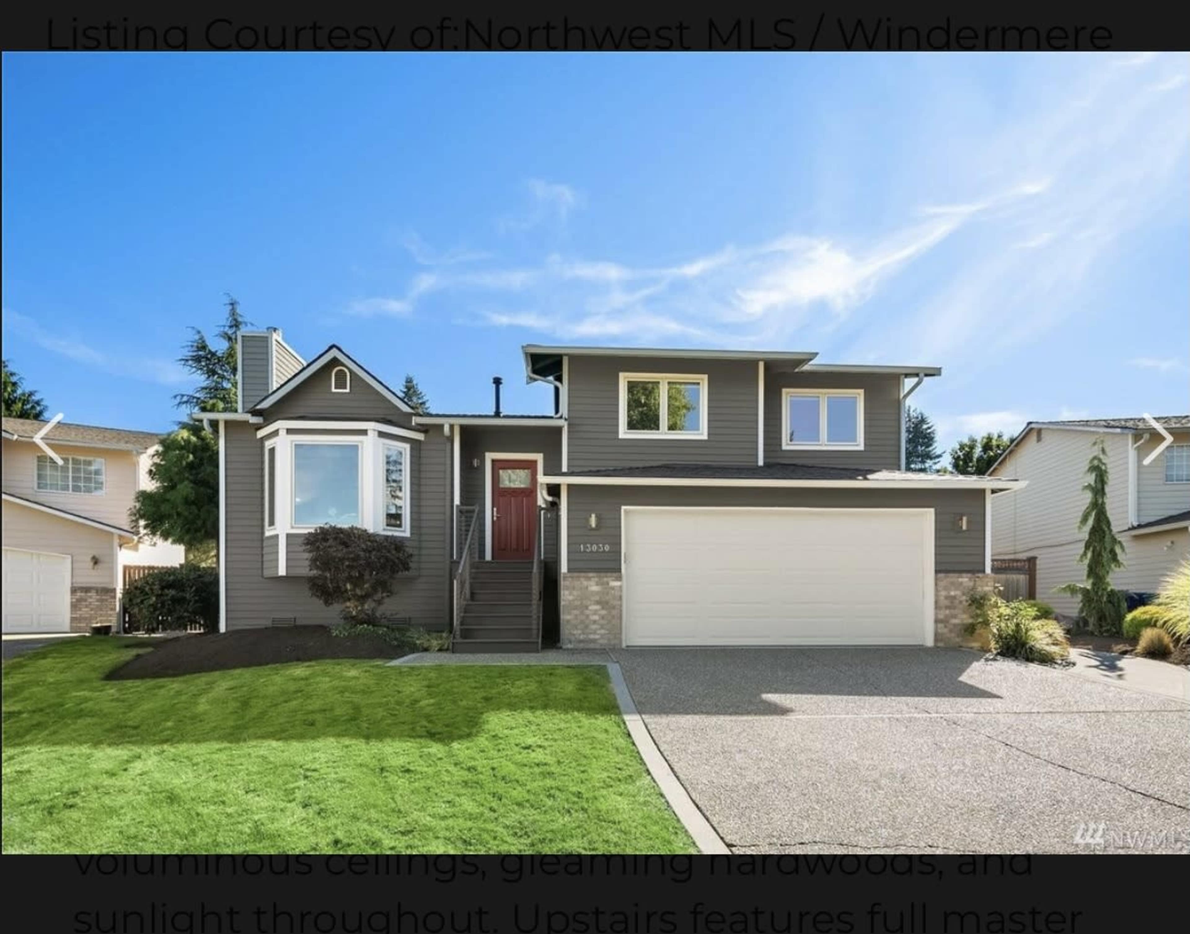 A modern two-story house with a dark exterior, large windows, and a neatly landscaped front yard.