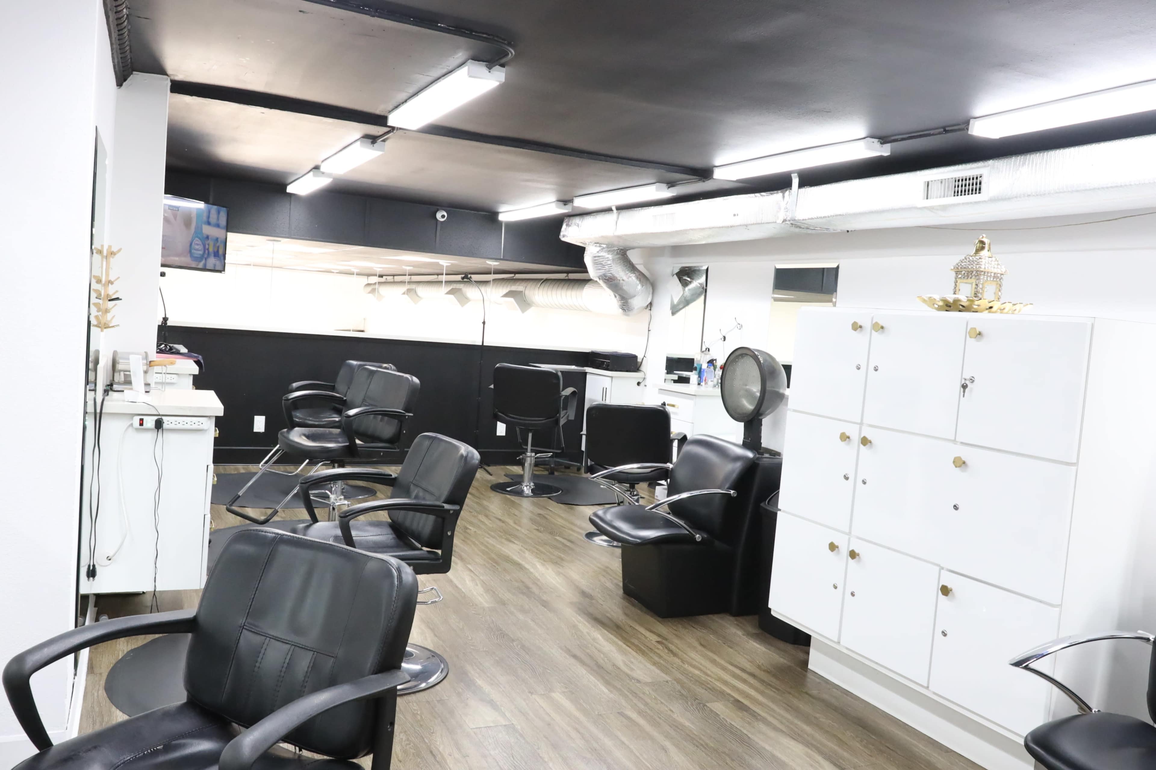 A hair salon interior with black styling chairs, a white storage cabinet, and overhead lighting.