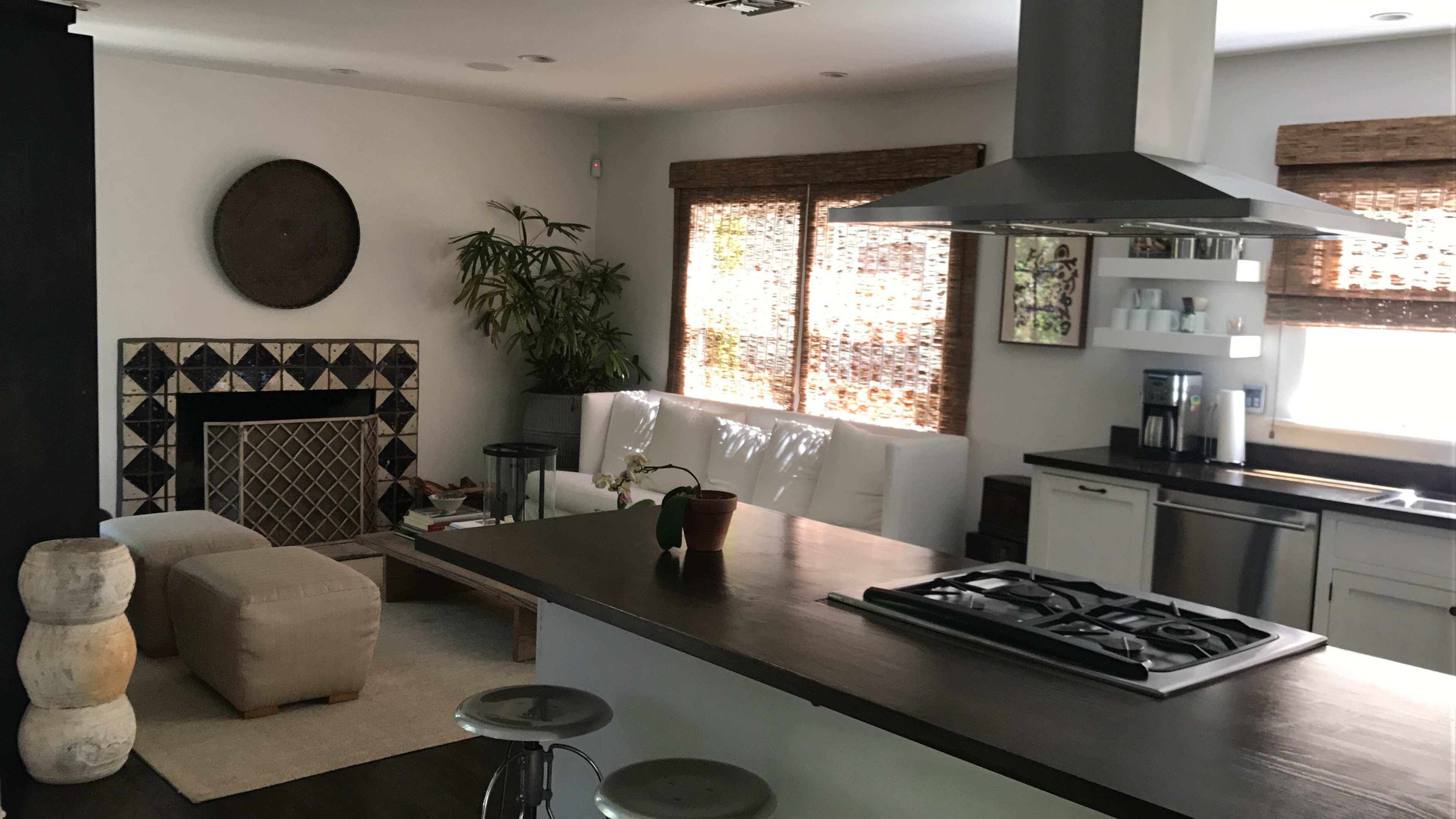 A modern kitchen and living area with a large island, a gas stove, a white sofa, and natural light streaming through window blinds.