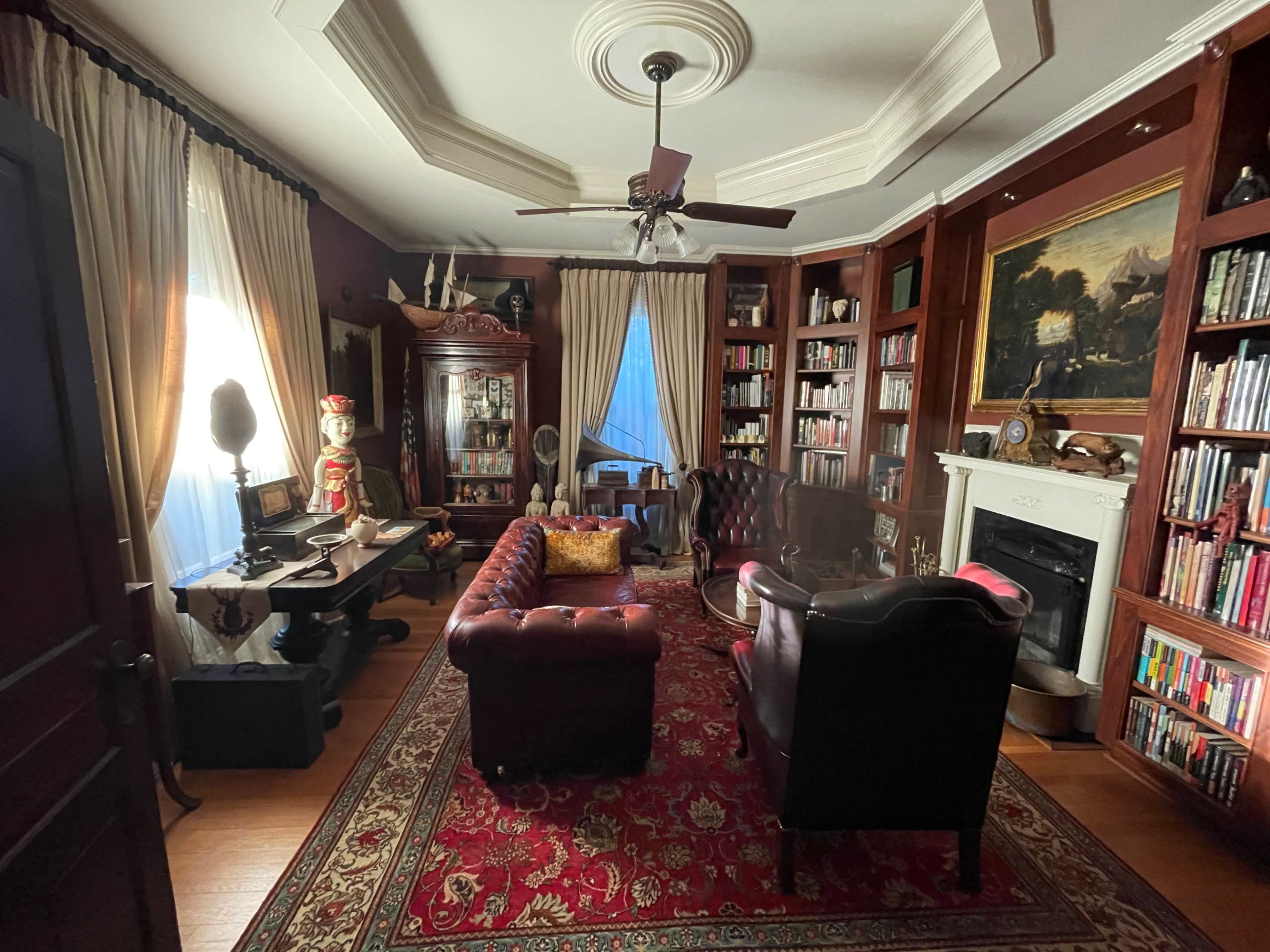 A vintage-style living room with dark wood bookshelves, a leather sofa, and a large ornate painting above a fireplace.