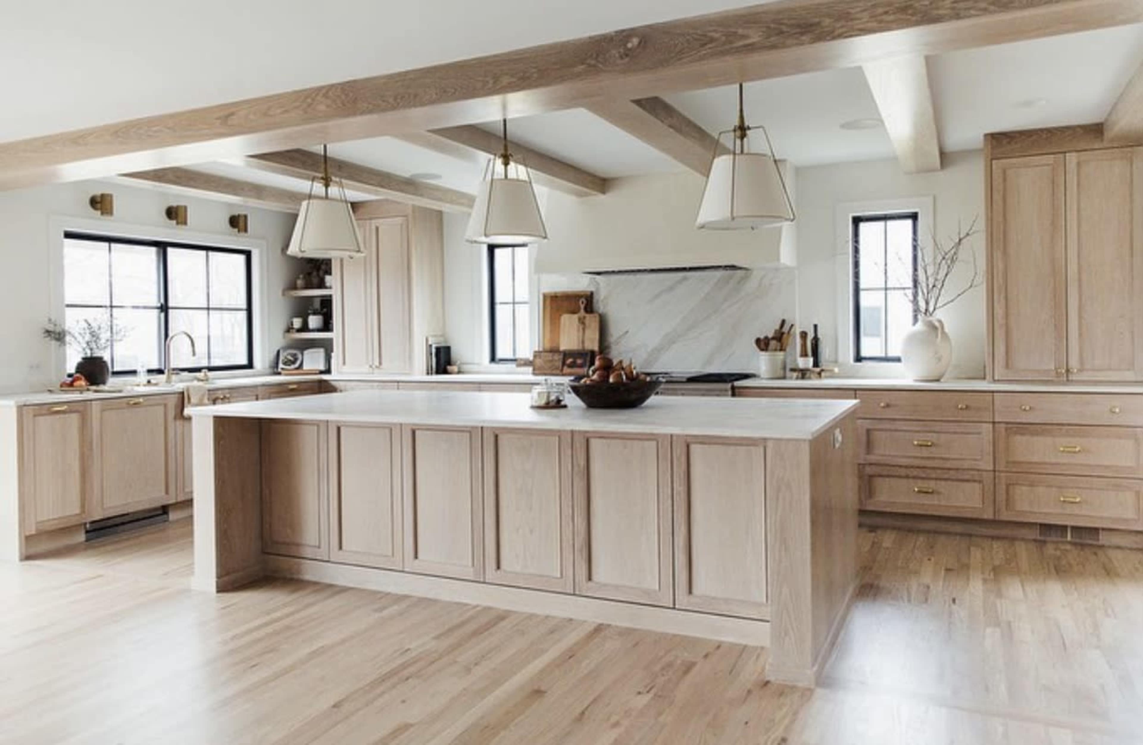 The kitchen features light wood cabinetry, a large island with a marble countertop, and pendant lighting.
