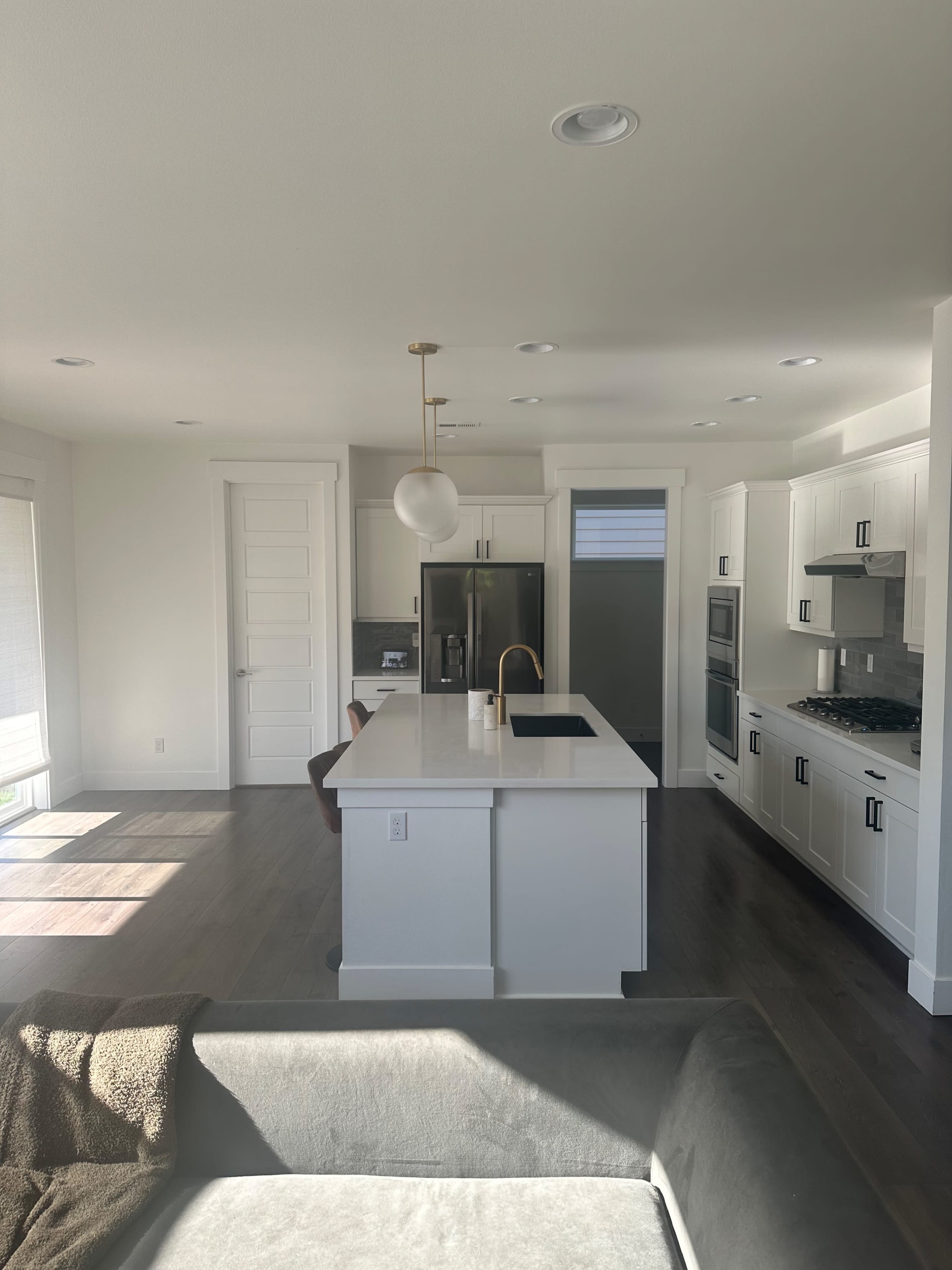 A modern kitchen featuring a central island with a sink, white cabinetry, stainless steel appliances, and large windows allowing natural light to enter the space.