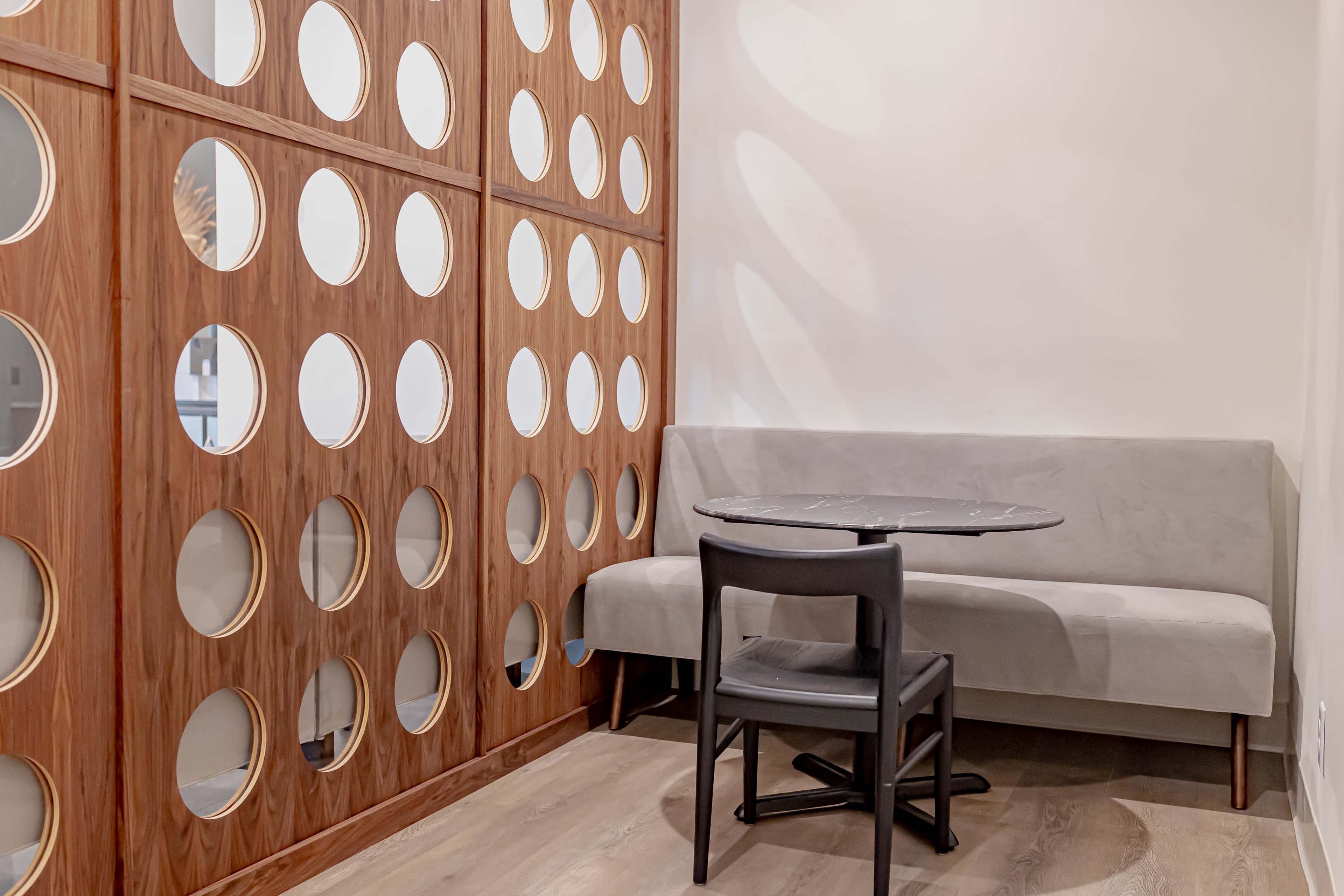 A small seating area features a bench and a round table, enclosed by a wooden wall with circular cutouts.
